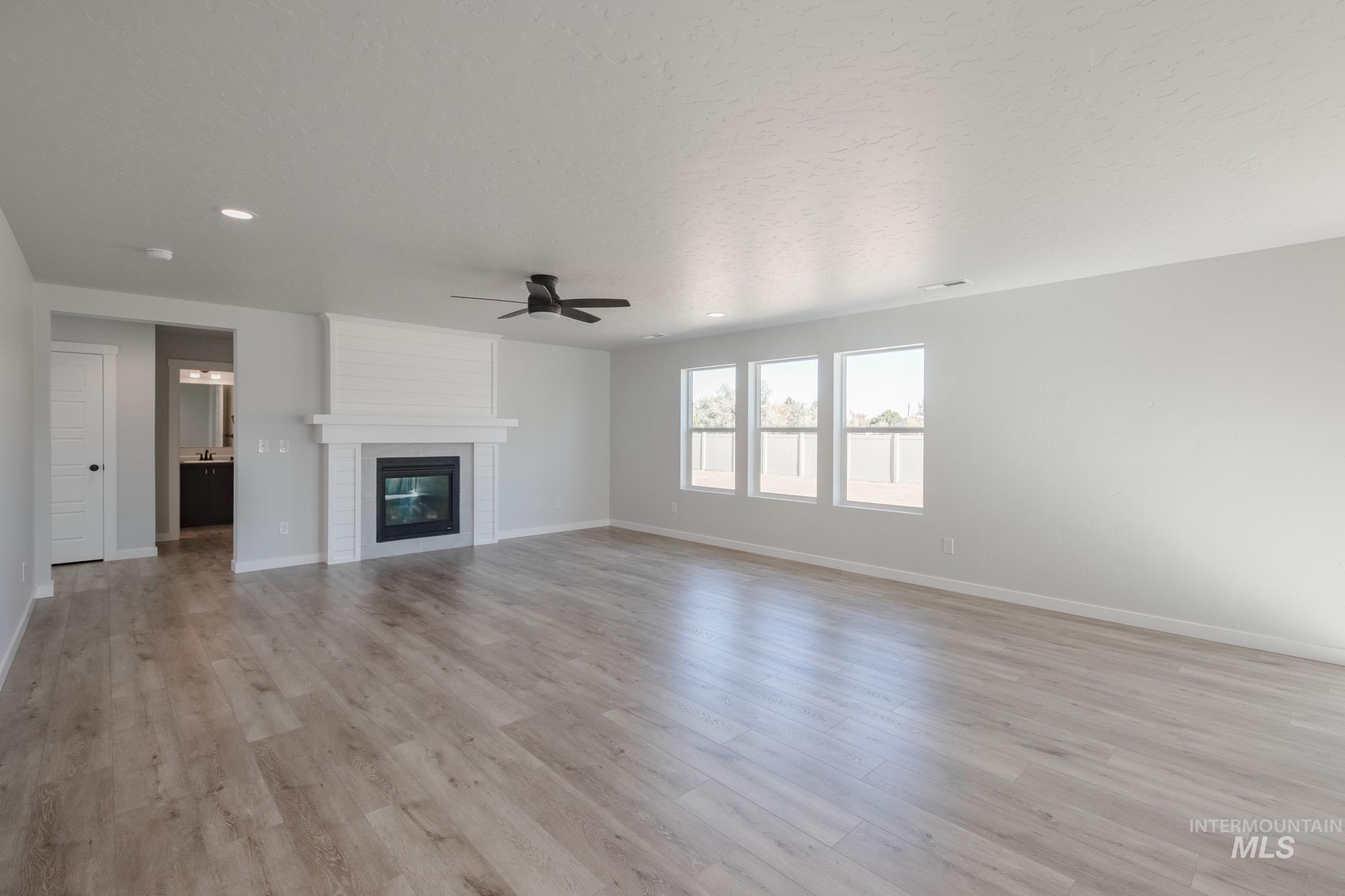 Unfurnished living room featuring light wood finished floors, a large fireplace, a ceiling fan, and a textured ceiling