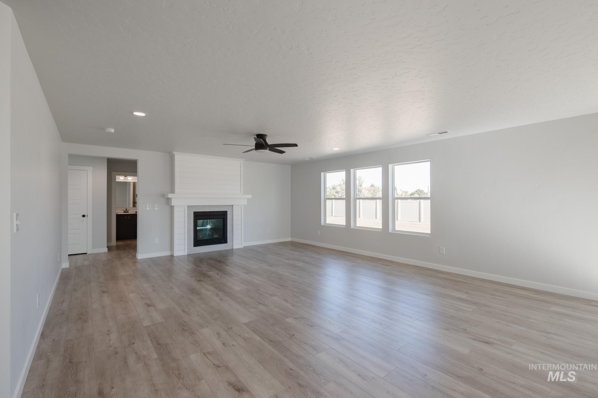 Unfurnished living room with light wood finished floors, a large fireplace, a ceiling fan, a textured ceiling, and recessed lighting