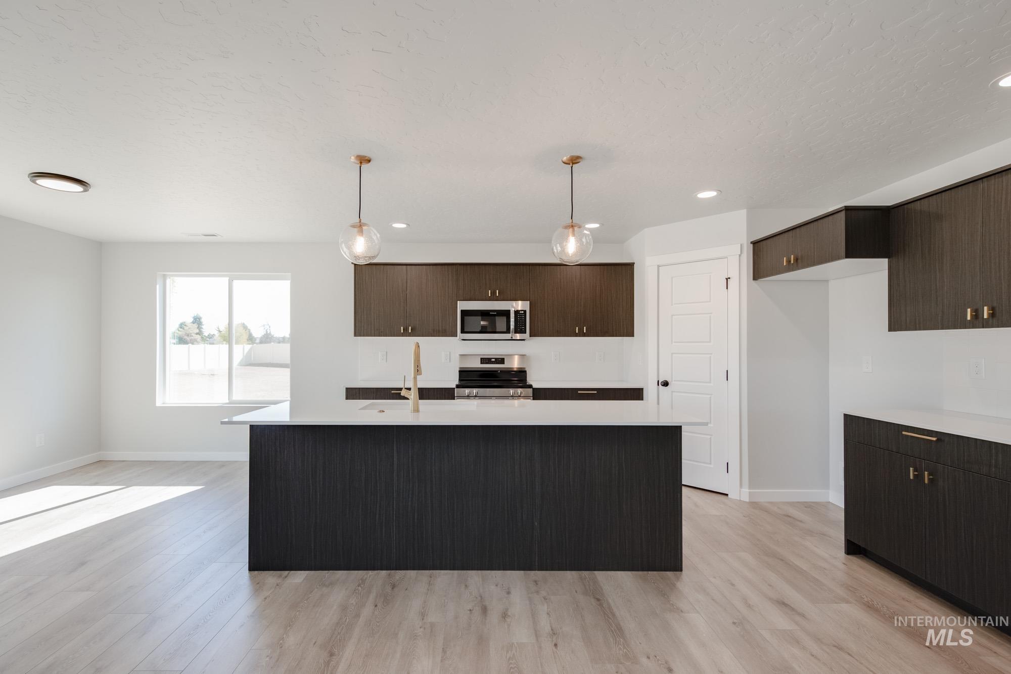 Kitchen featuring dark brown cabinets, decorative light fixtures, appliances with stainless steel finishes, light wood finished floors, and recessed lighting