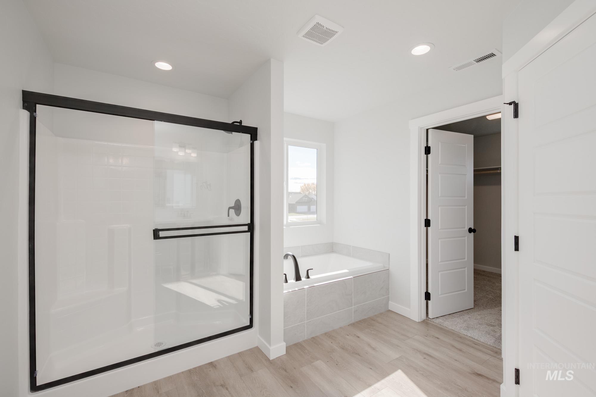 Bathroom featuring light wood-style flooring, a stall shower, a bath, recessed lighting, and a walk in closet