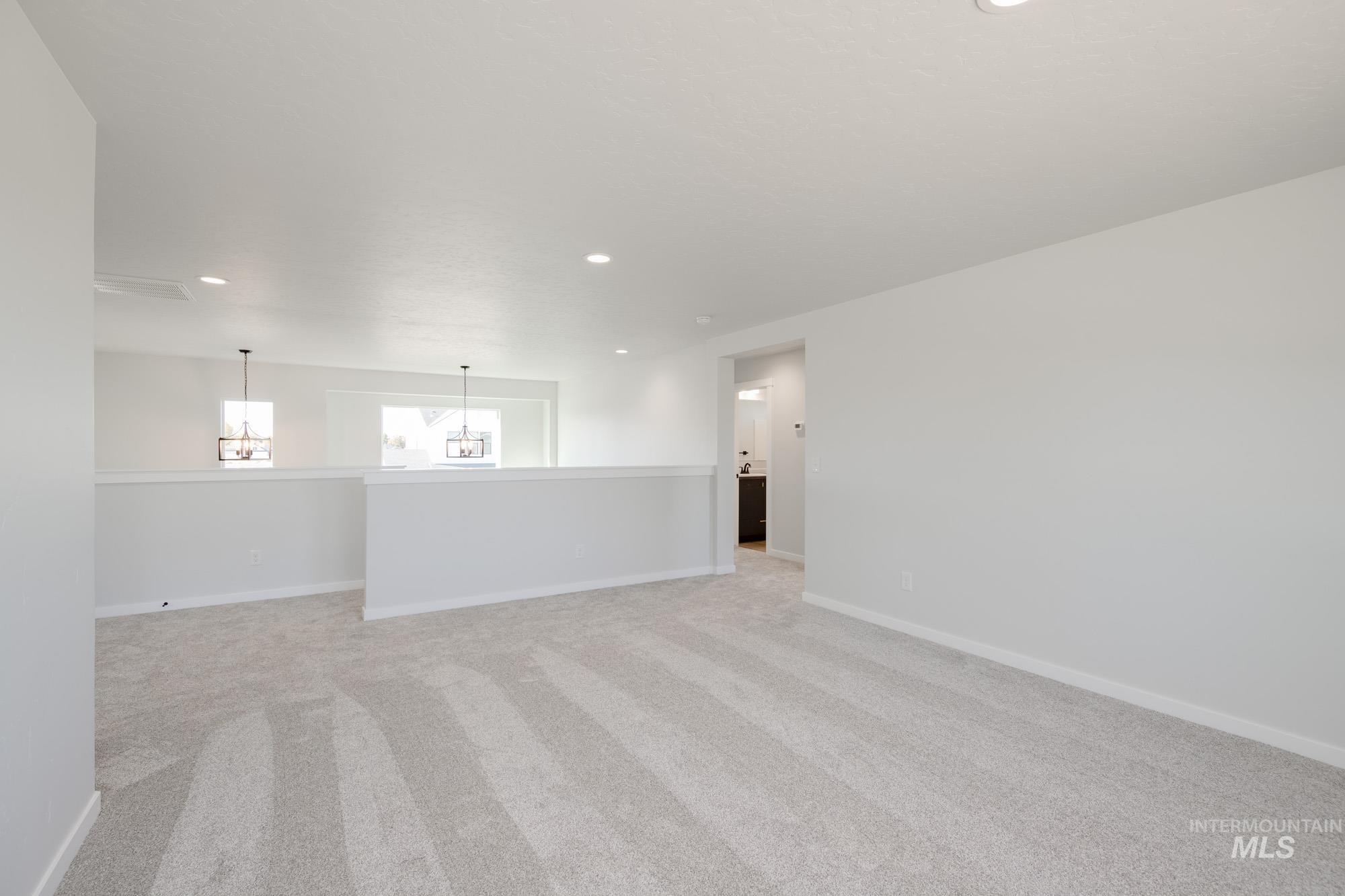 Empty room with light colored carpet, recessed lighting, and a chandelier