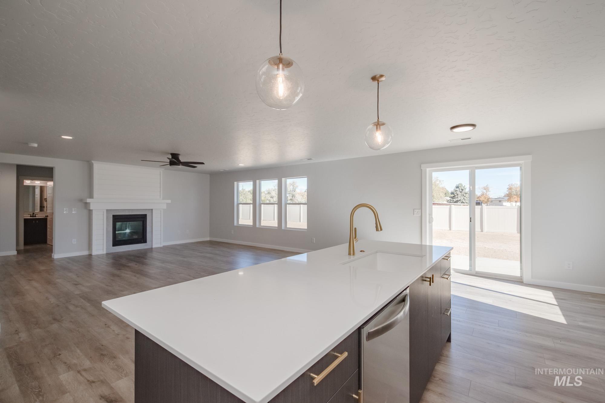 Kitchen featuring a center island with sink, decorative light fixtures, open floor plan, a large fireplace, and stainless steel dishwasher