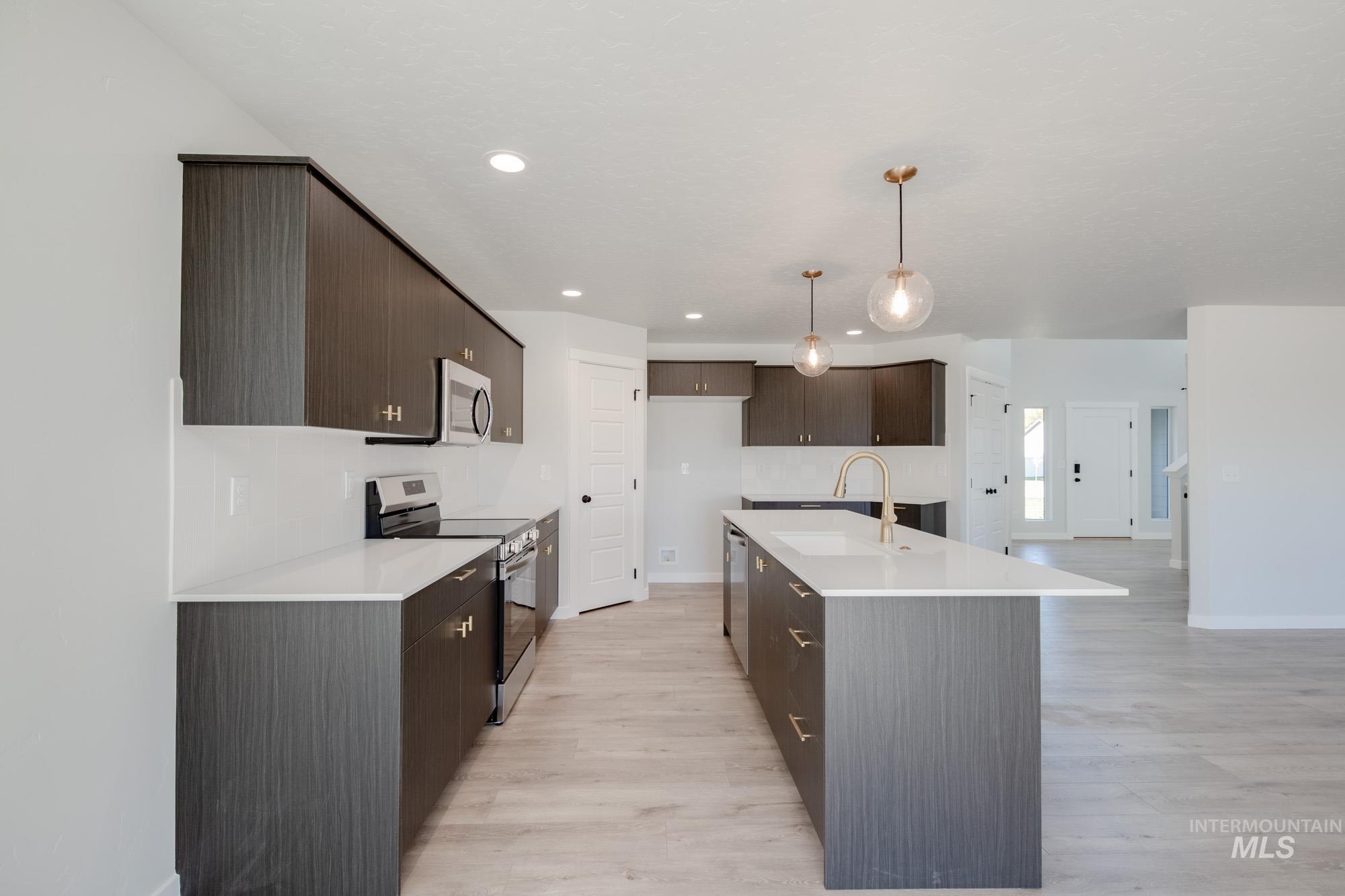 Kitchen featuring stainless steel appliances, dark brown cabinets, pendant lighting, light wood-style floors, and recessed lighting