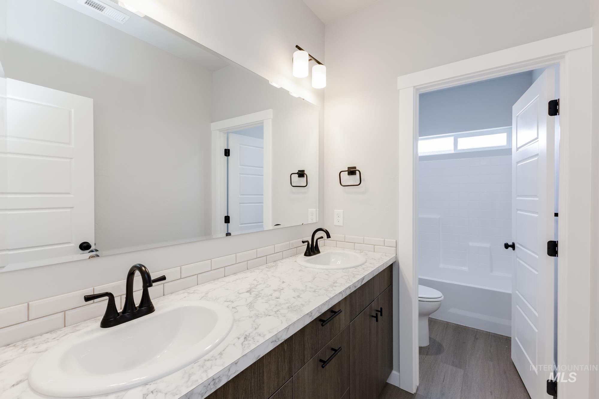Bathroom featuring double vanity, dark wood finished floors, and  shower combination