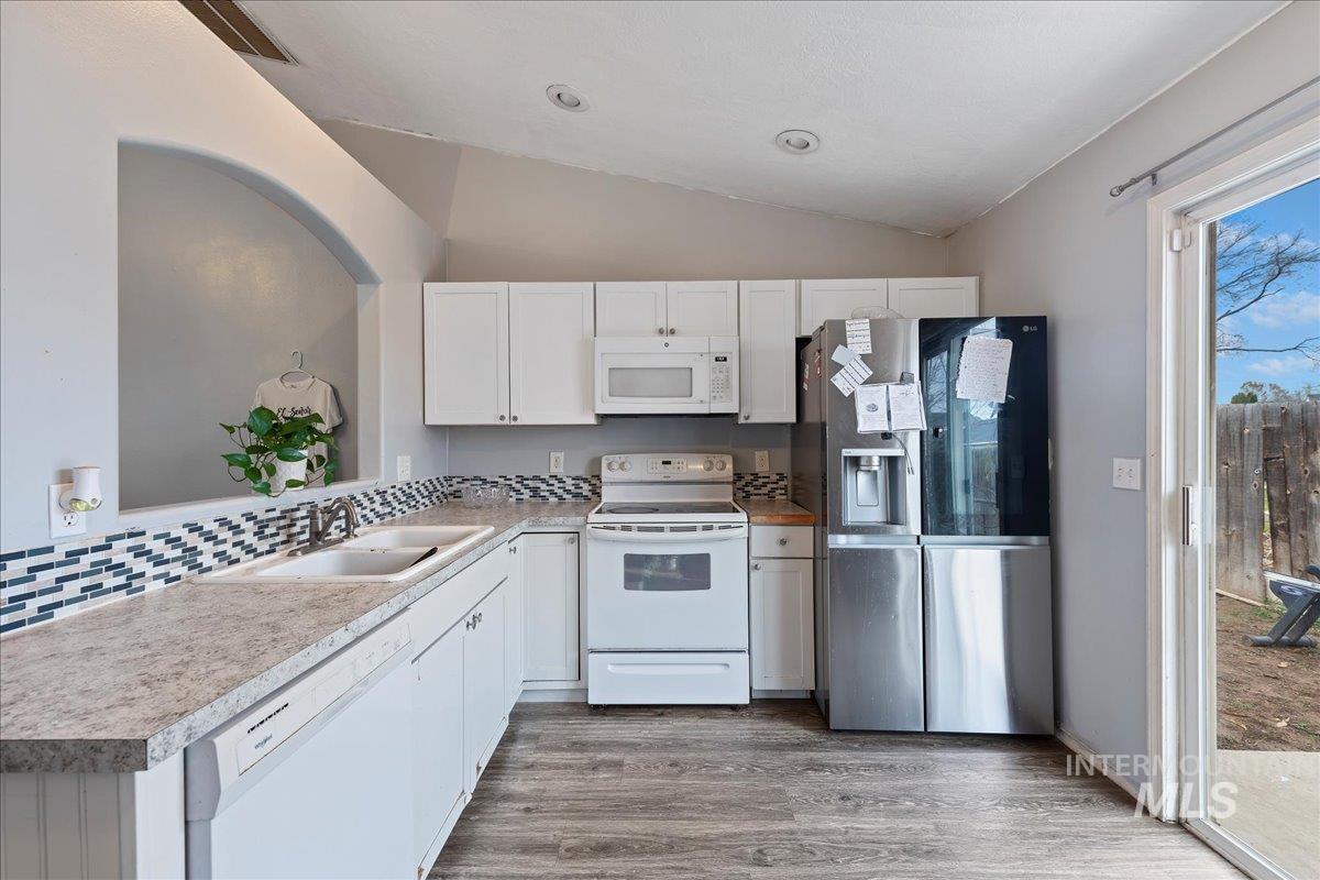 Kitchen with lofted ceiling, white cabinets, white appliances, dark wood-style floors, and light countertops