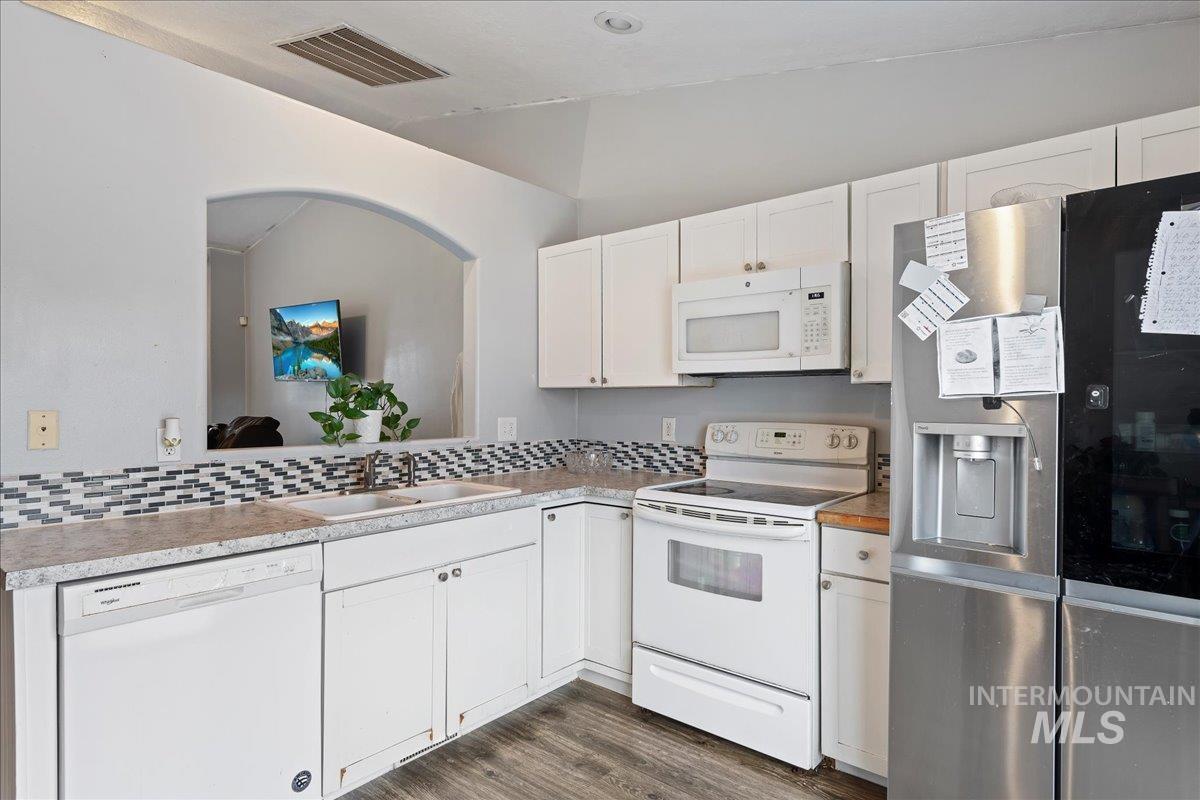Kitchen with white appliances, white cabinetry, dark wood finished floors, light countertops, and vaulted ceiling