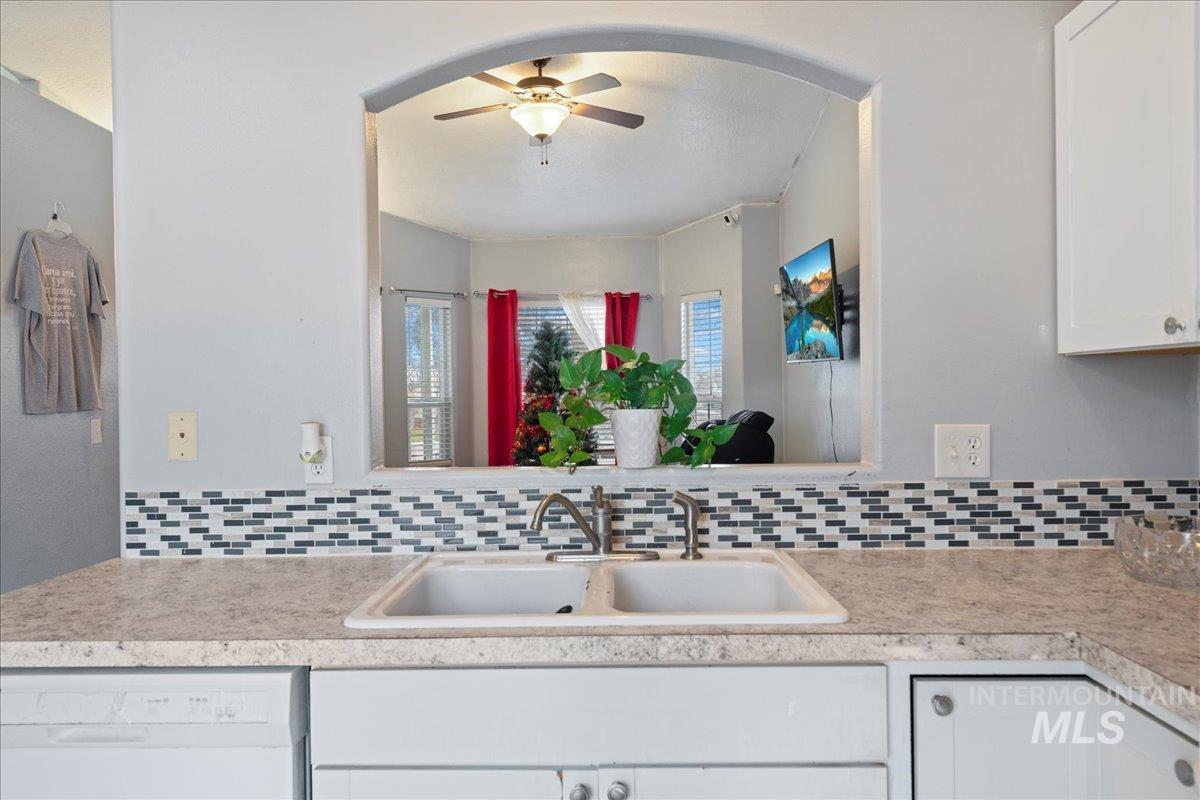 Kitchen featuring white dishwasher, light countertops, white cabinetry, ceiling fan, and decorative backsplash