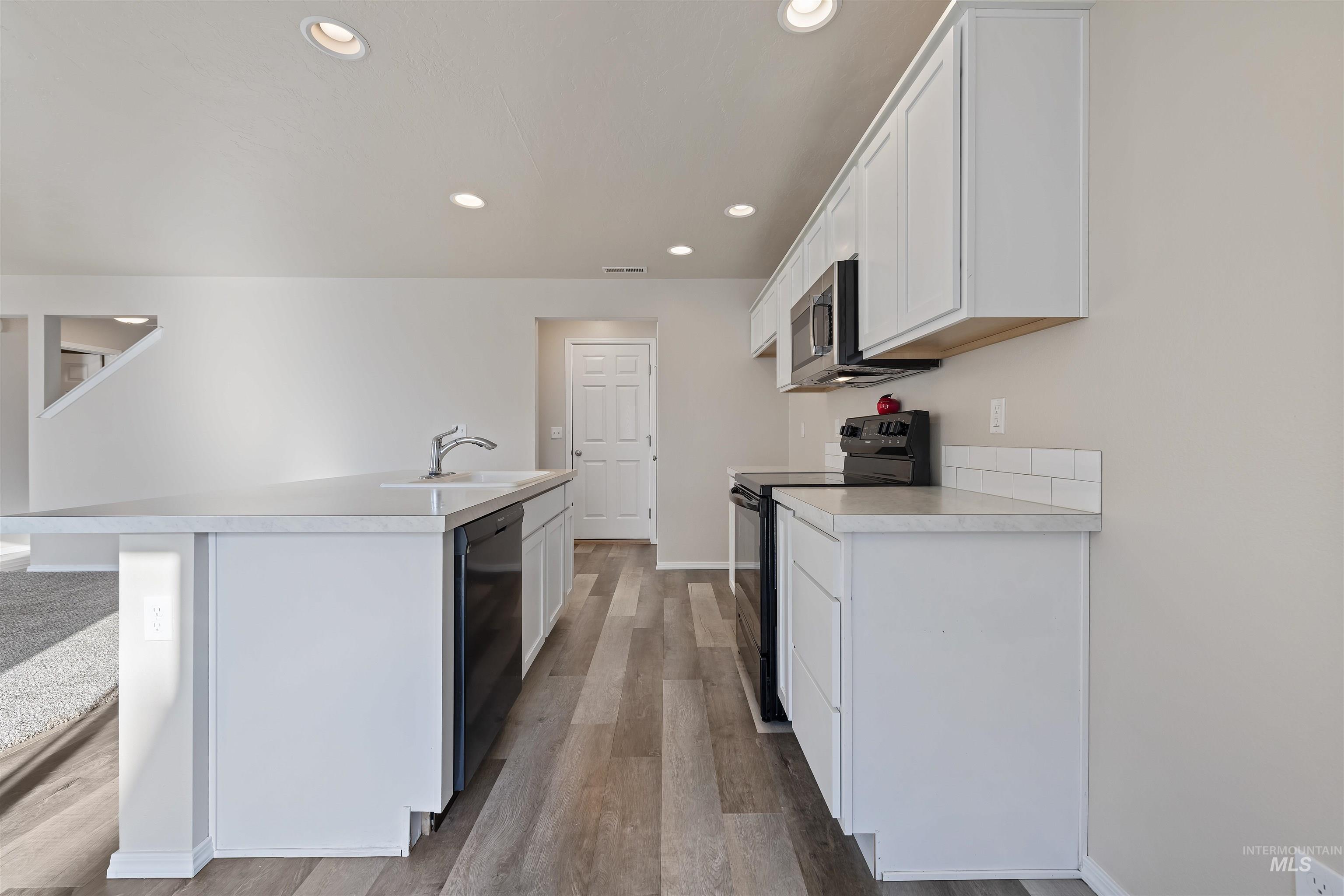 Kitchen featuring black appliances, white cabinetry, light countertops, recessed lighting, and a kitchen island with sink