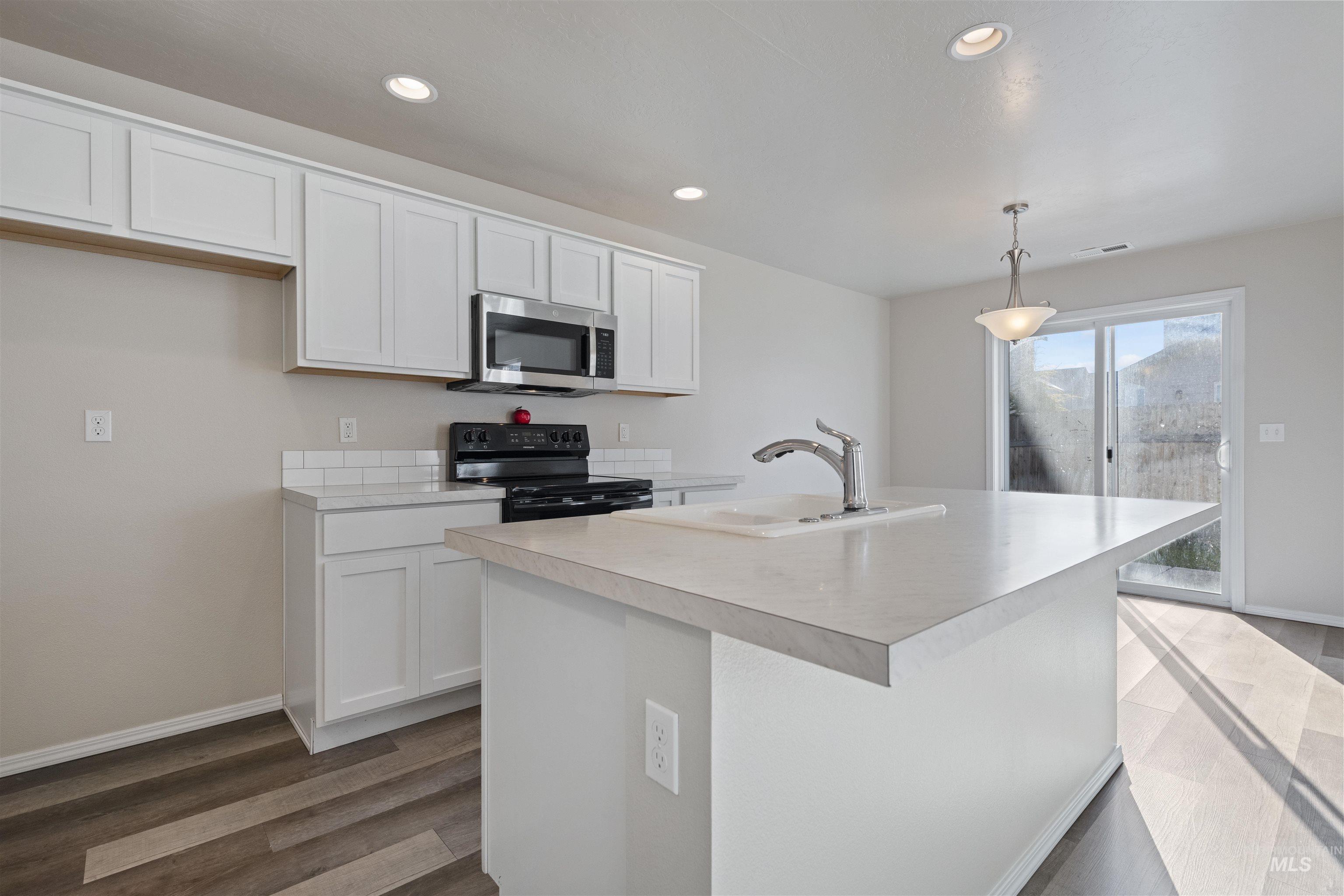 Kitchen with black electric range oven, white cabinetry, light countertops, stainless steel microwave, and hanging light fixtures