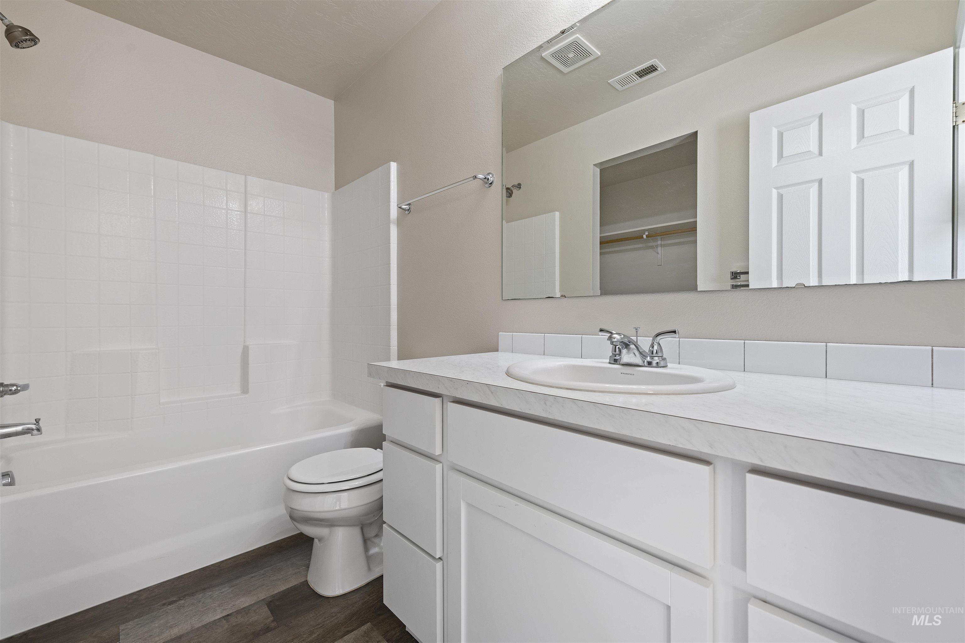 Bathroom featuring vanity, tub / shower combination, dark wood finished floors, and a spacious closet