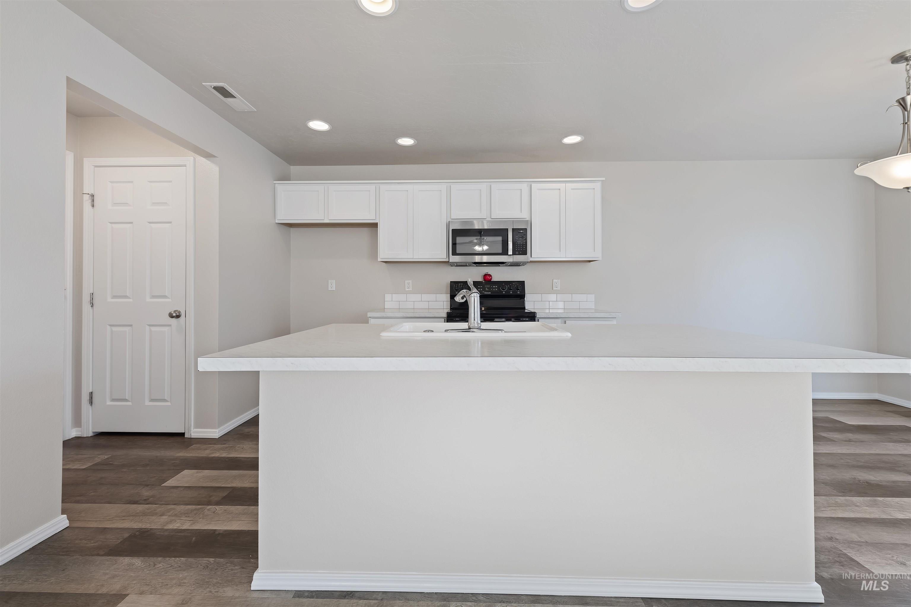 Kitchen featuring white cabinets, light countertops, stainless steel microwave, electric range, and recessed lighting