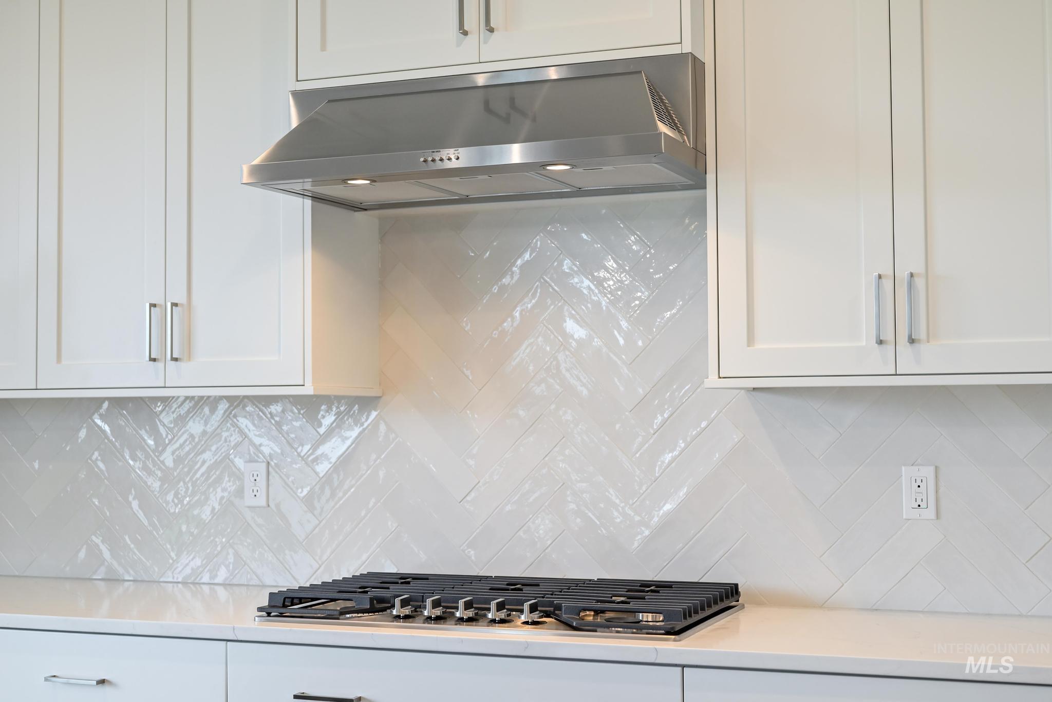 Kitchen featuring decorative backsplash, under cabinet range hood, white cabinets, and light stone counters