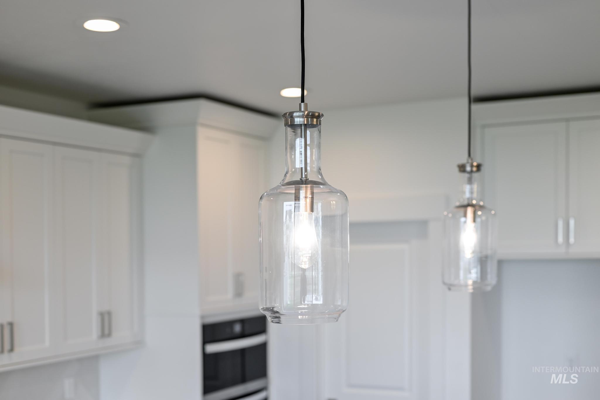 Kitchen view of white cabinetry, wall oven, decorative light fixtures, and recessed lighting