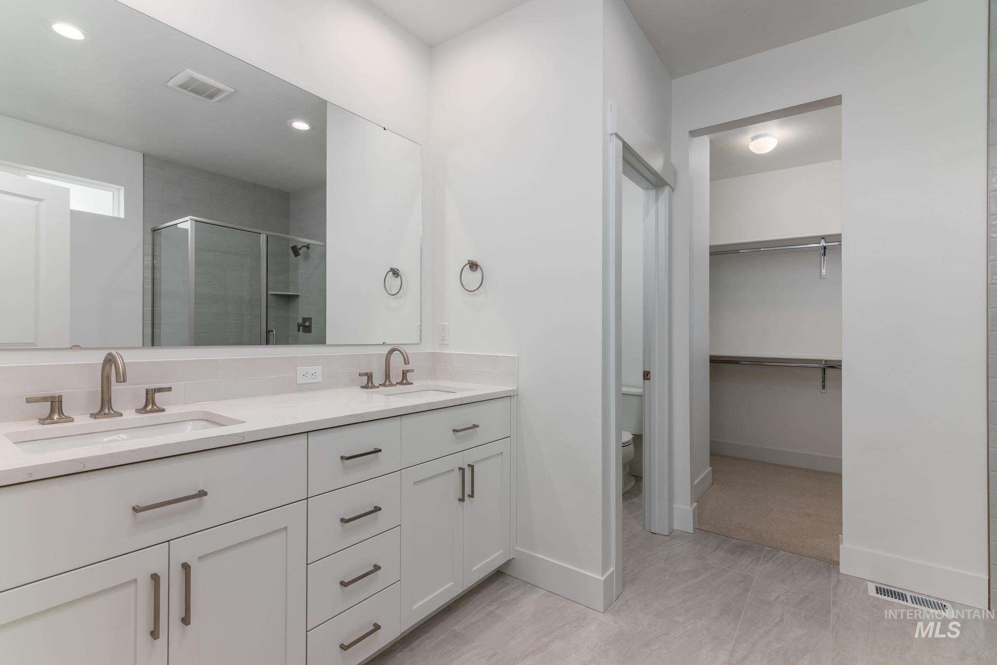 Bathroom featuring a stall shower, double vanity, a walk in closet, and recessed lighting