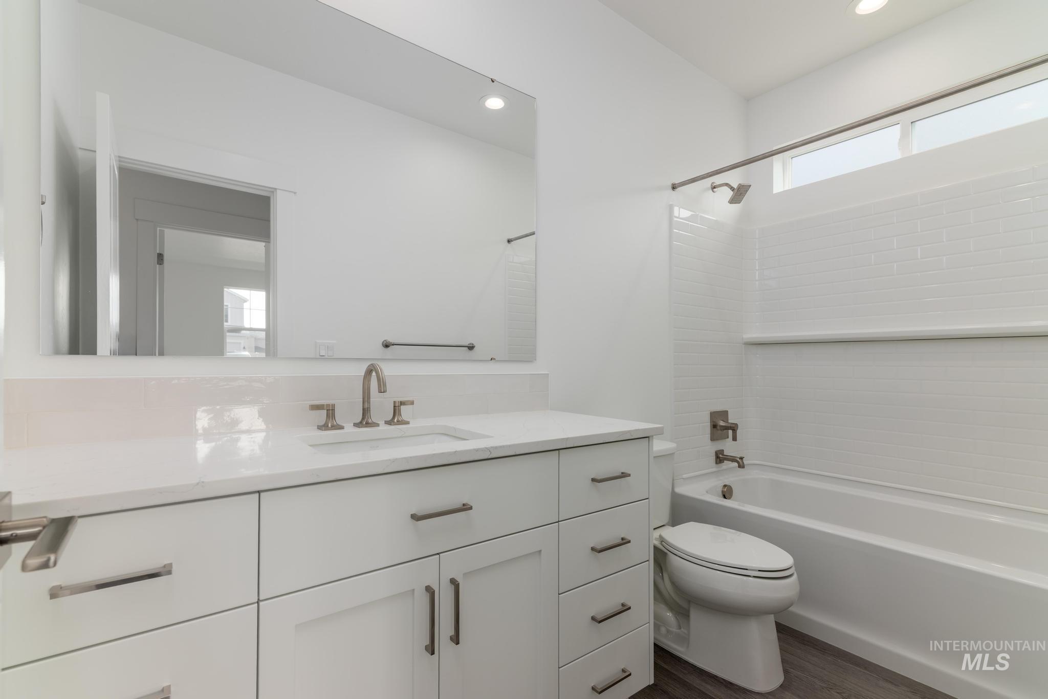 Bathroom with vanity, washtub / shower combination, dark wood finished floors, and recessed lighting