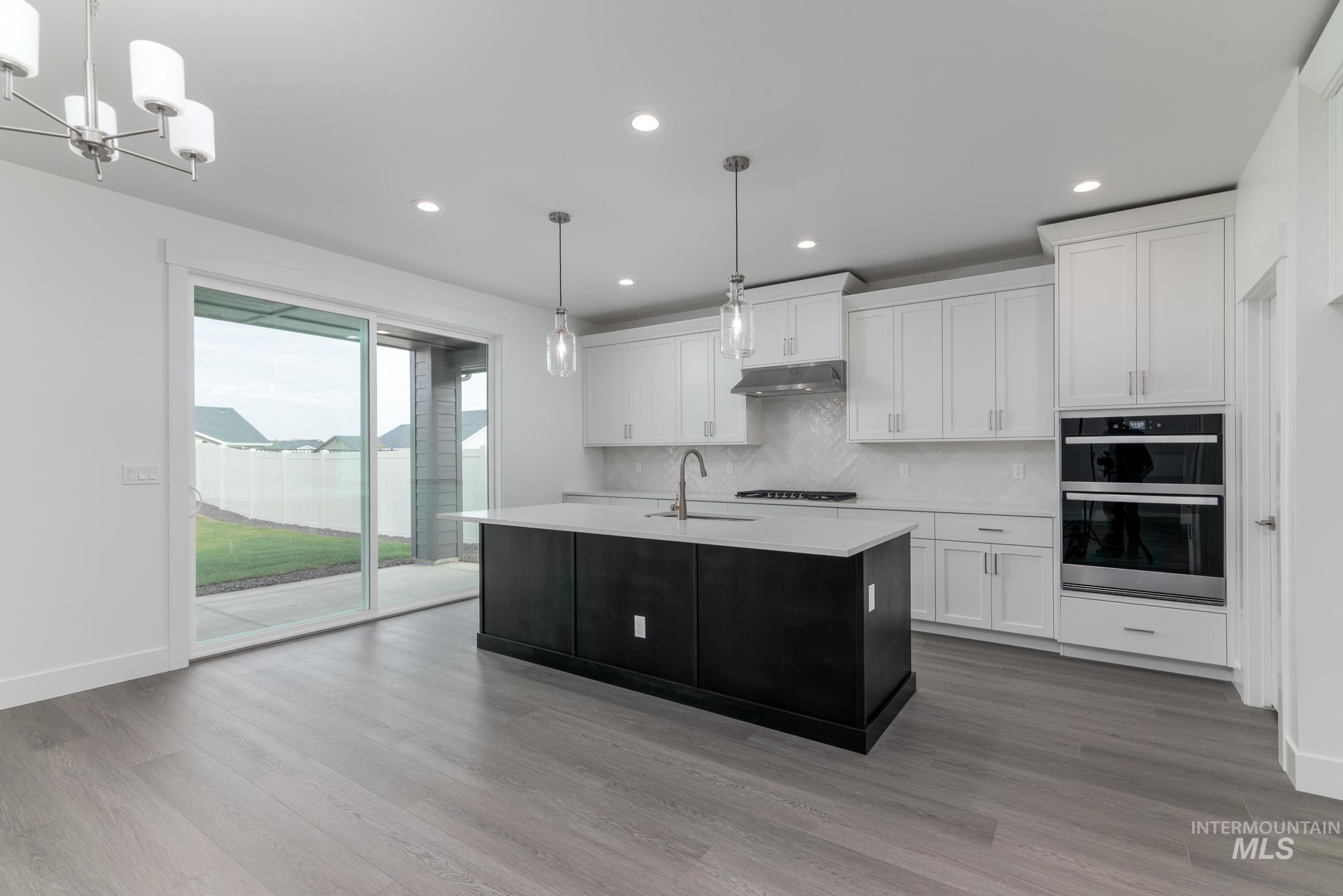 Kitchen featuring white cabinetry, pendant lighting, a center island with sink, dark cabinetry, and double wall oven