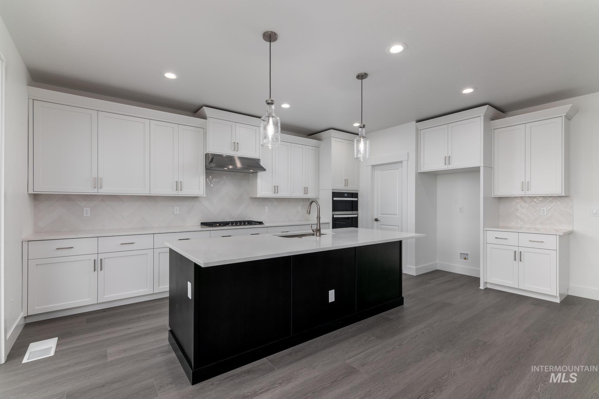 Kitchen with backsplash, dark cabinets, hanging light fixtures, a kitchen island with sink, and recessed lighting