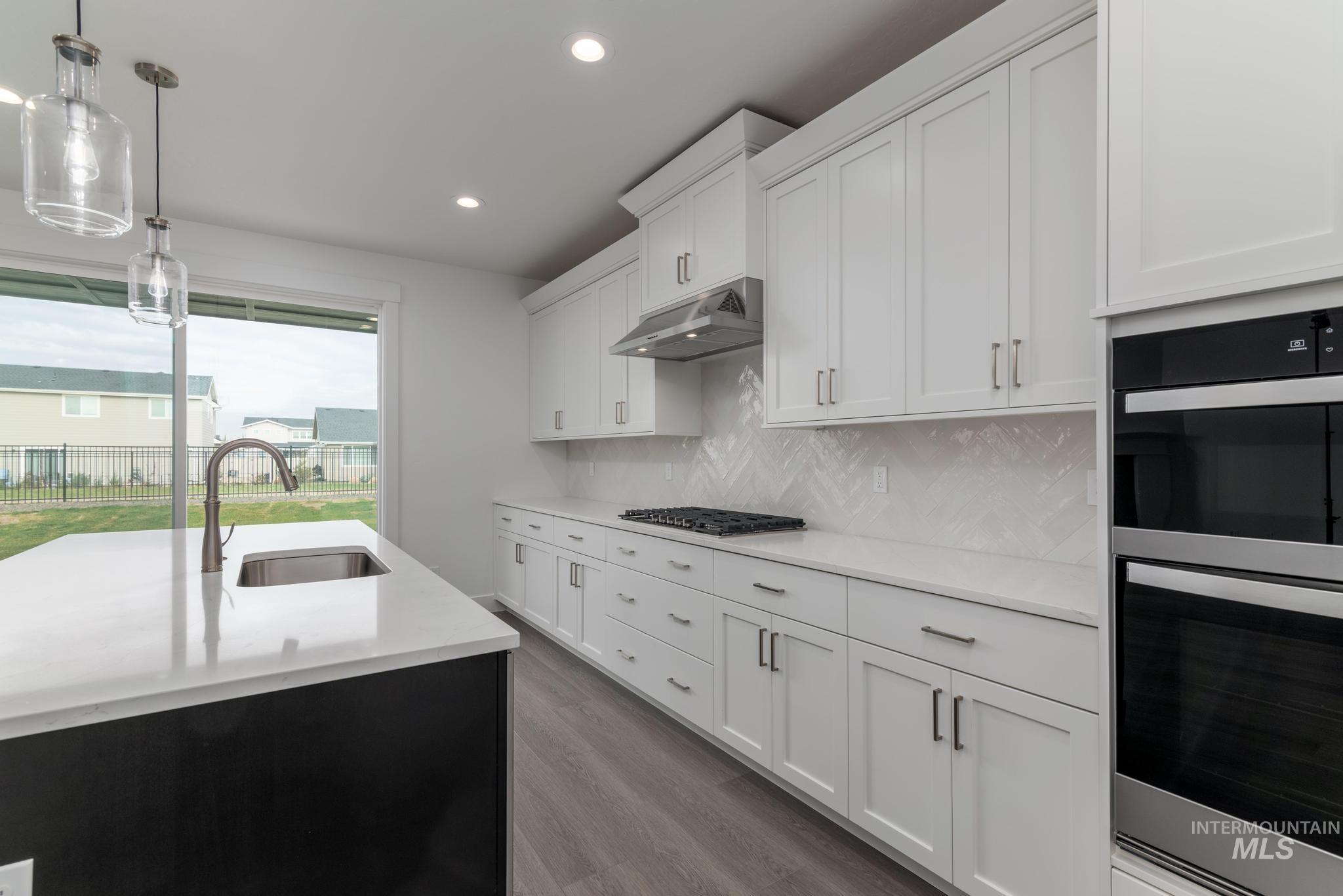 Kitchen featuring appliances with stainless steel finishes, decorative light fixtures, white cabinetry, tasteful backsplash, and under cabinet range hood