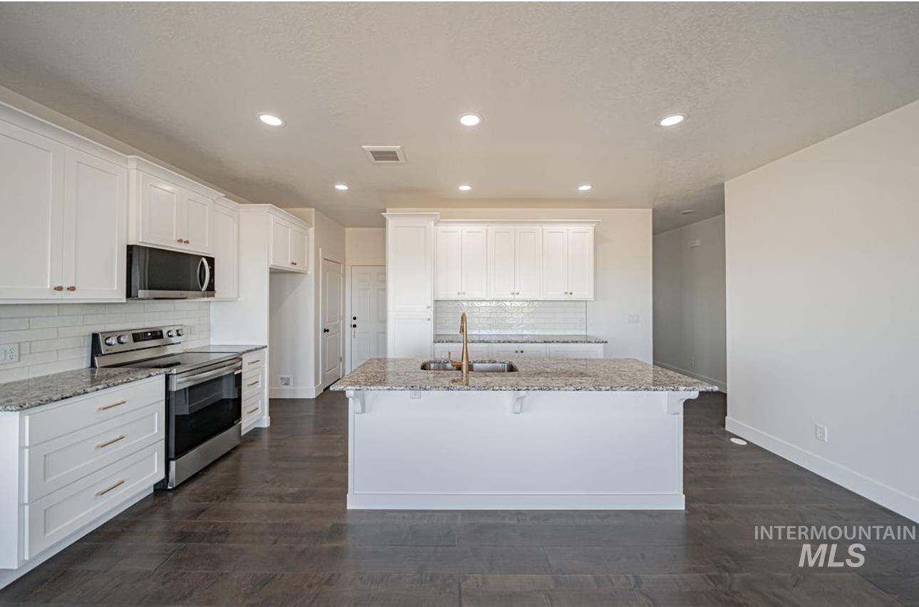 Kitchen with stainless steel appliances, light stone counters, white cabinets, recessed lighting, and a center island with sink