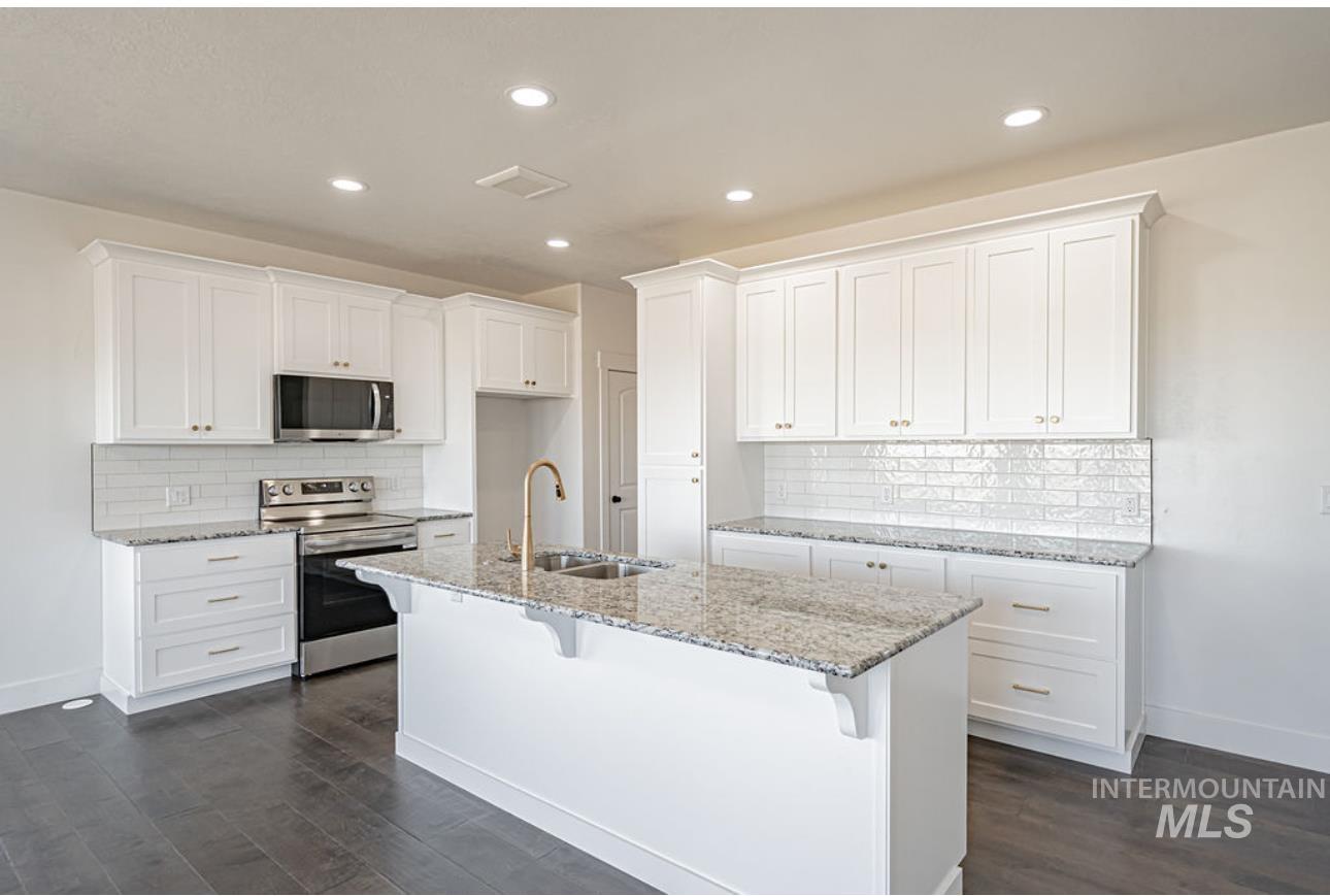 Kitchen with appliances with stainless steel finishes, a kitchen breakfast bar, white cabinets, light stone counters, and dark wood finished floors