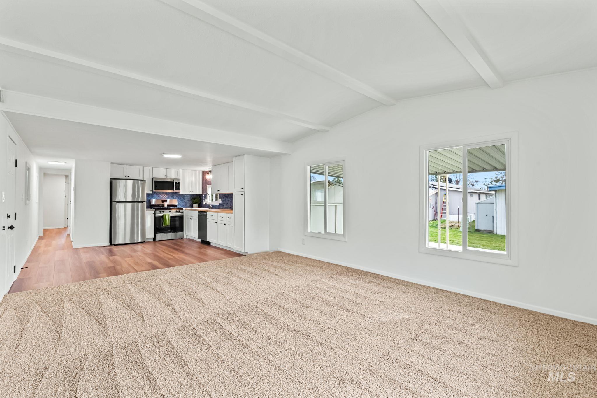 Unfurnished living room with beamed ceiling and light colored carpet