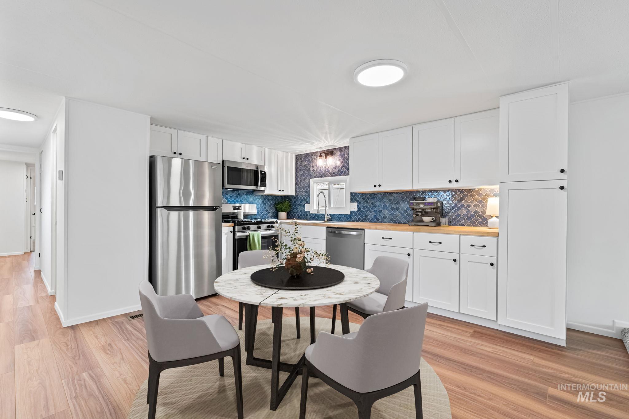 Kitchen featuring appliances with stainless steel finishes, white cabinetry, light wood-style floors, and butcher block countertops