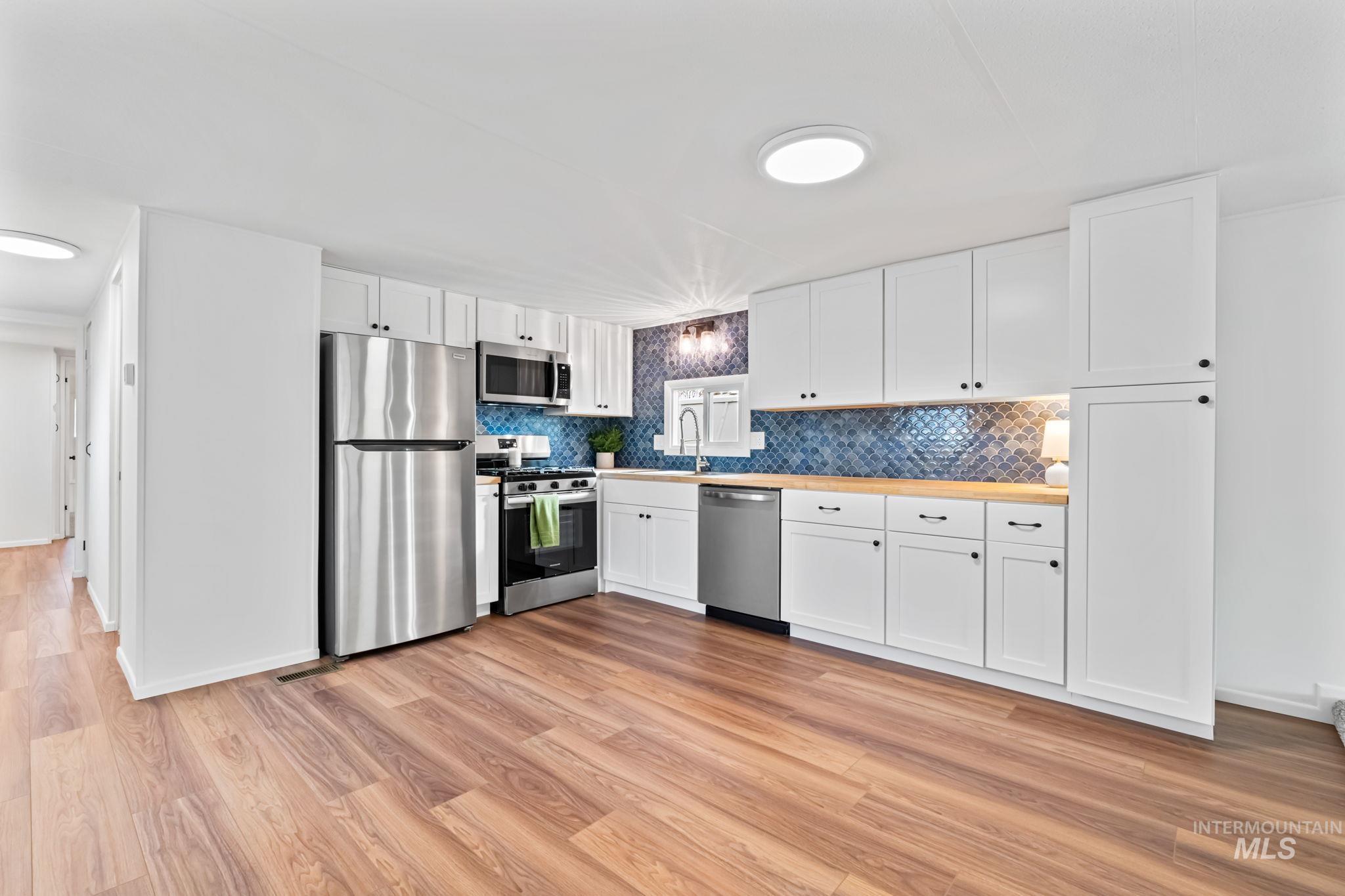 Kitchen featuring white cabinetry, stainless steel appliances, light wood-style flooring, light countertops, and decorative backsplash