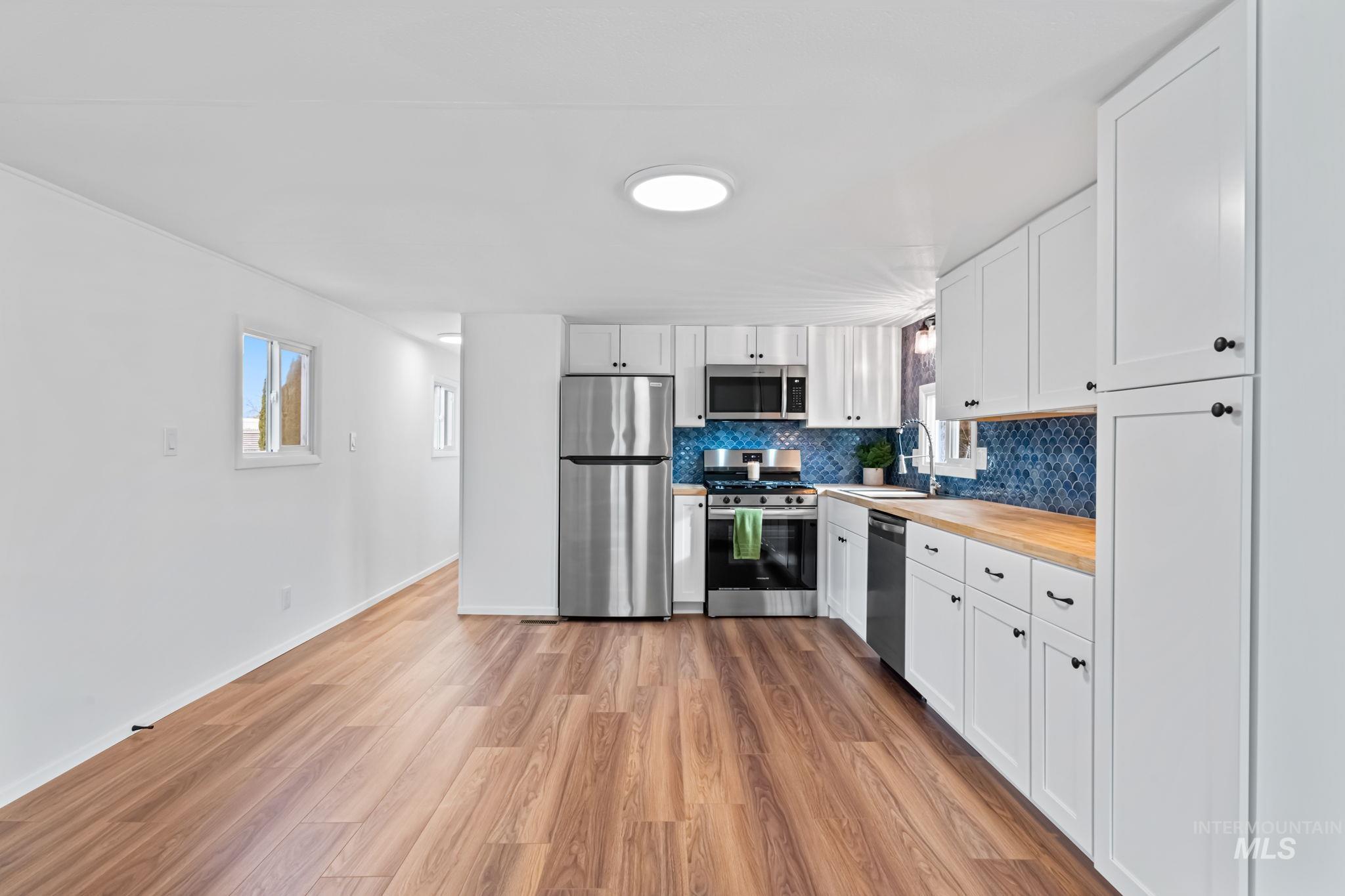 Kitchen featuring white cabinets, light wood finished floors, appliances with stainless steel finishes, butcher block counters, and decorative backsplash
