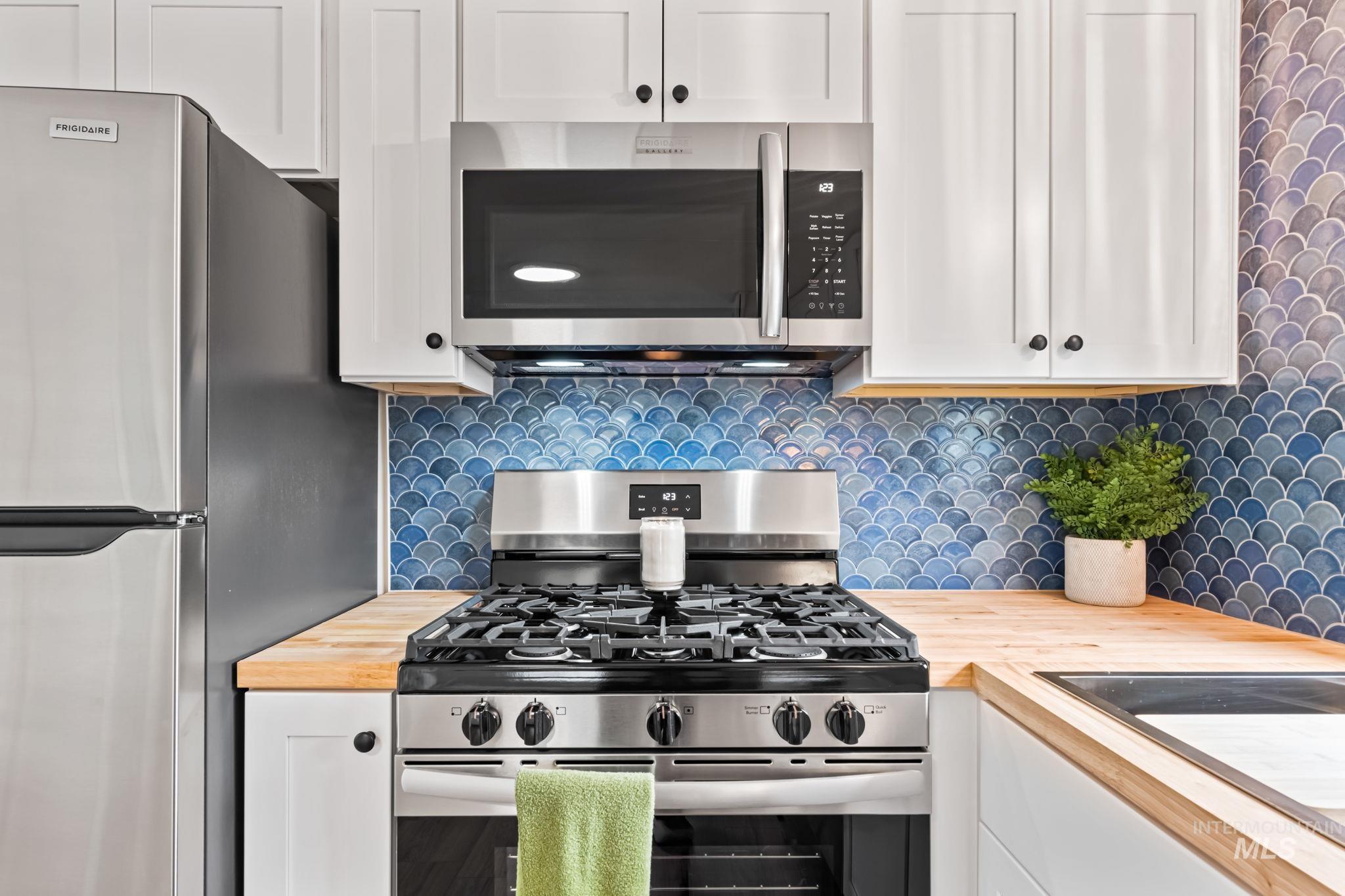 Kitchen with stainless steel appliances, white cabinetry, butcher block countertops, and backsplash