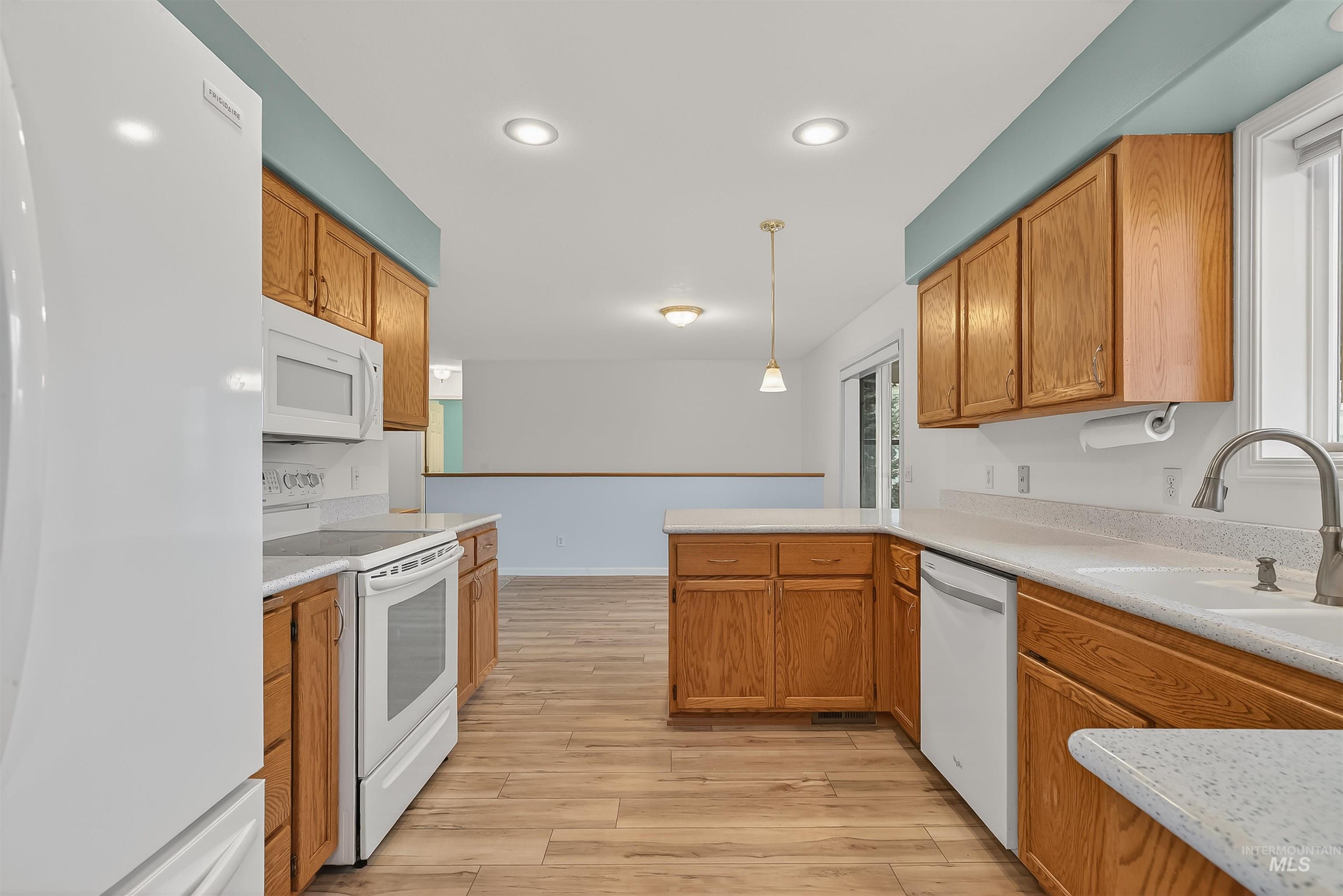 Kitchen with white appliances, decorative light fixtures, light wood finished floors, brown cabinetry, and recessed lighting