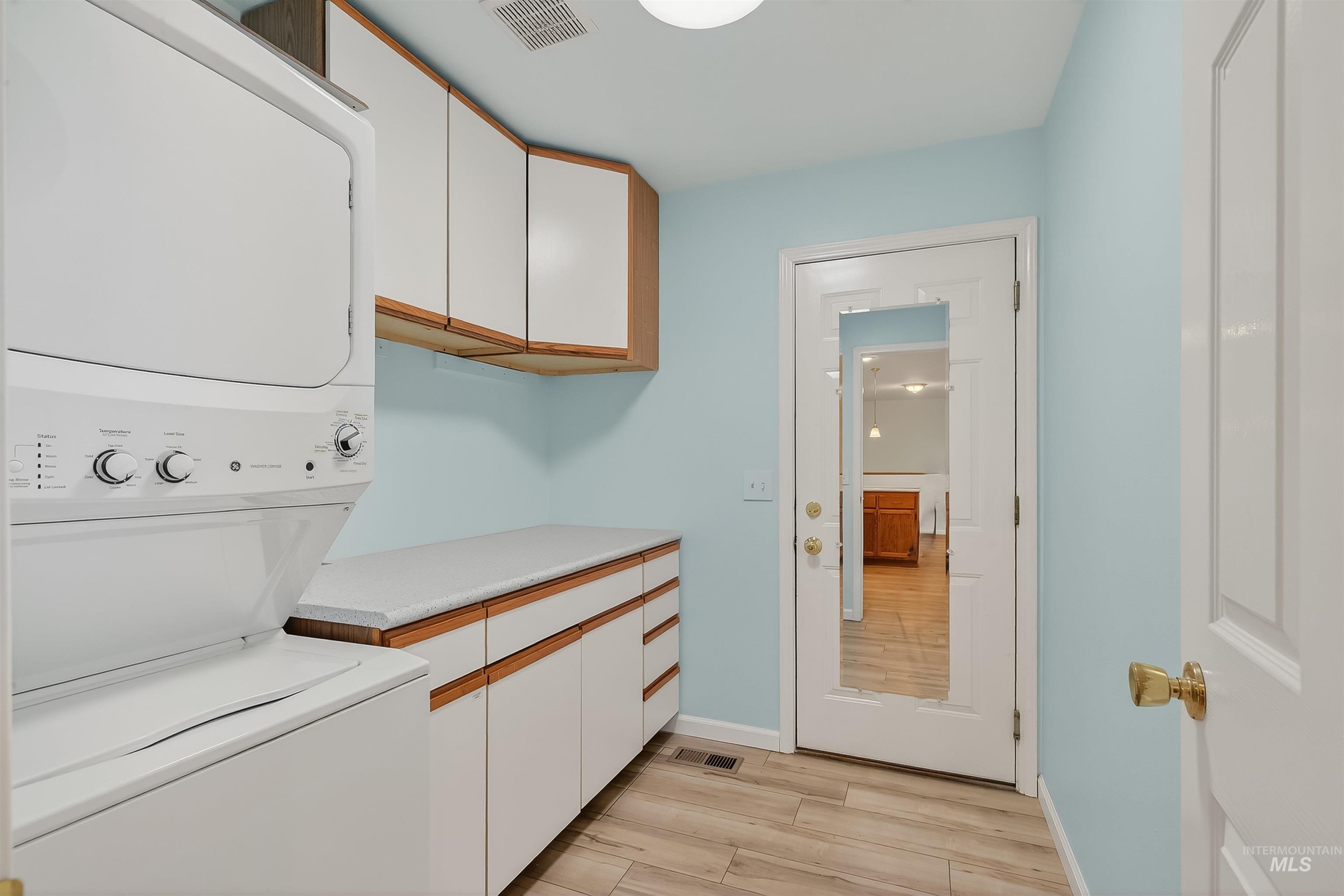 Laundry area featuring cabinet space, light wood-style flooring, and stacked washer / drying machine