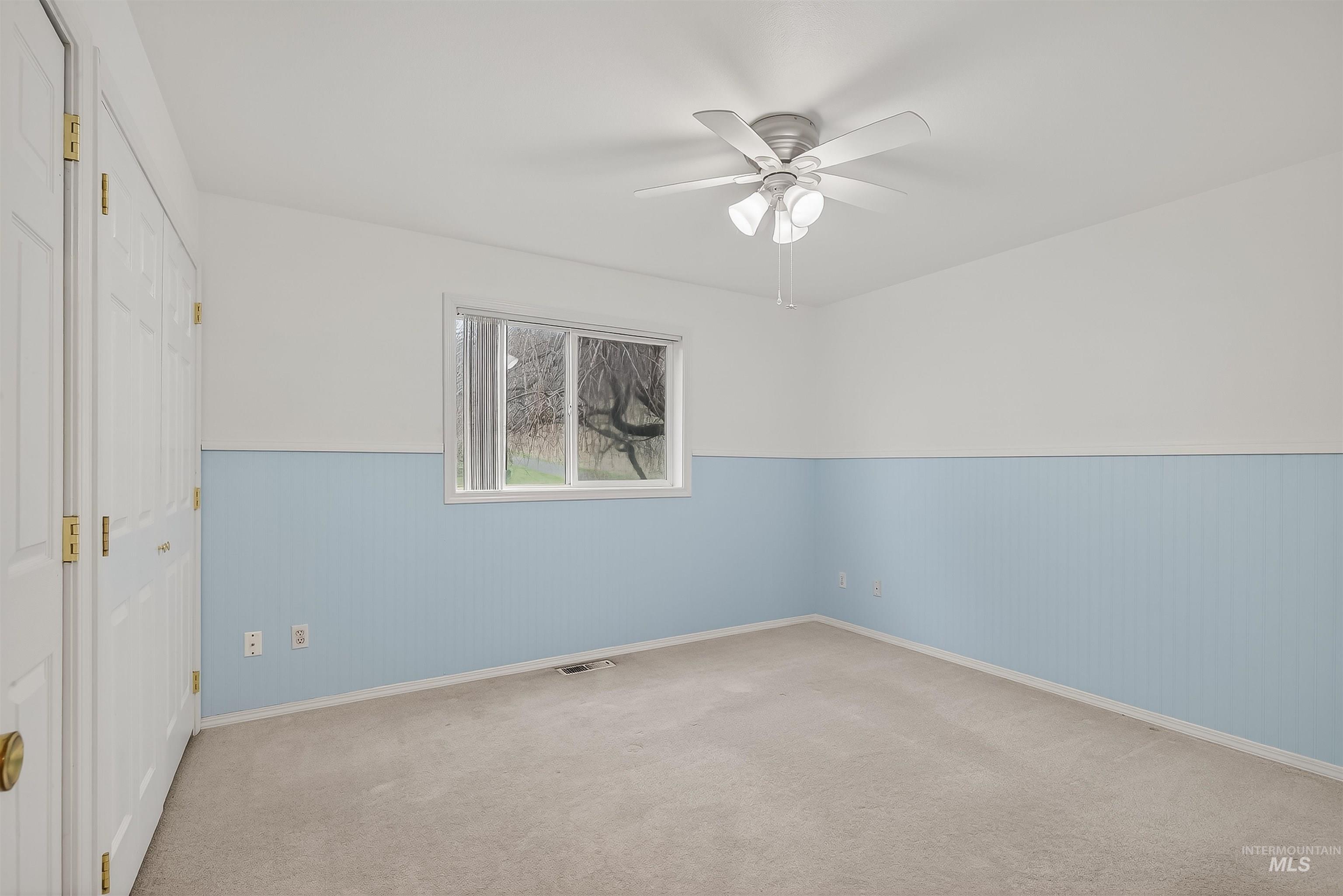 Carpeted empty room featuring wainscoting, a ceiling fan, and wood walls