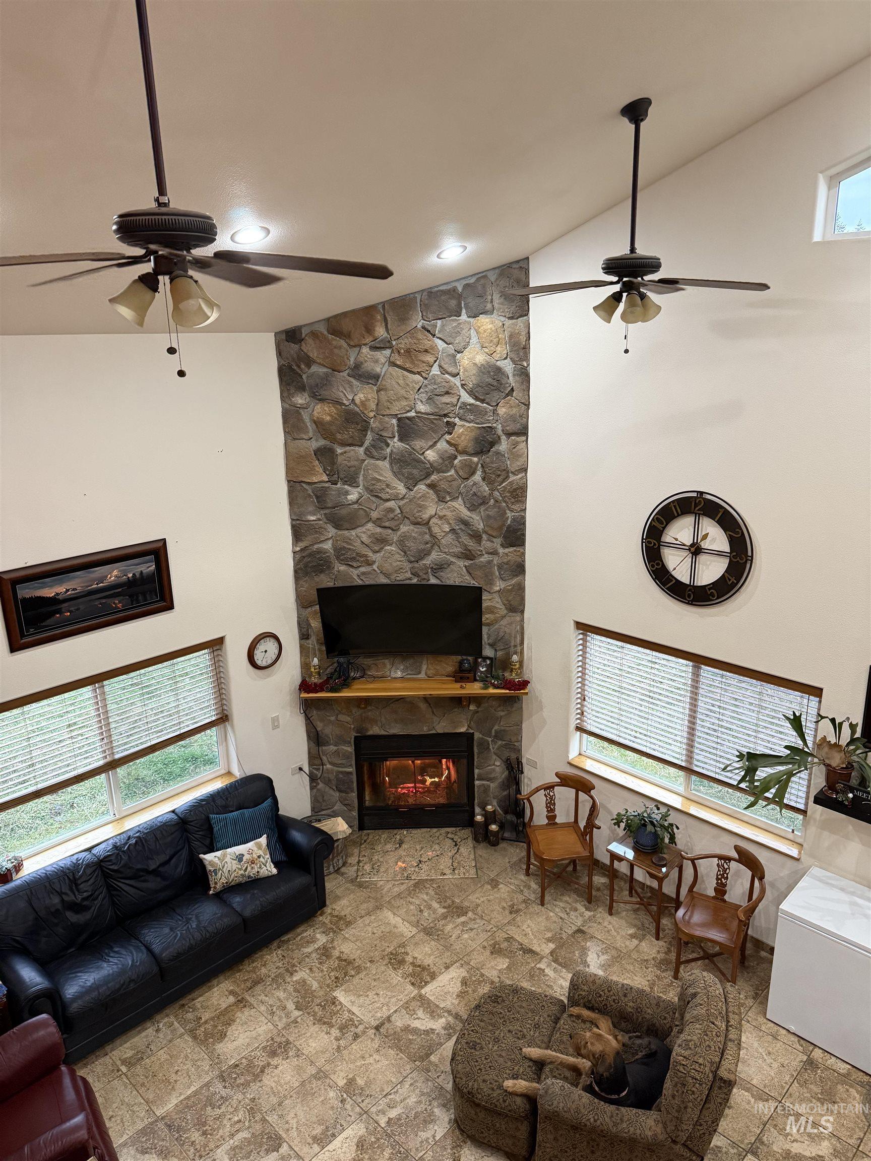 Living area featuring high vaulted ceiling, a ceiling fan, a fireplace, and stone finish flooring