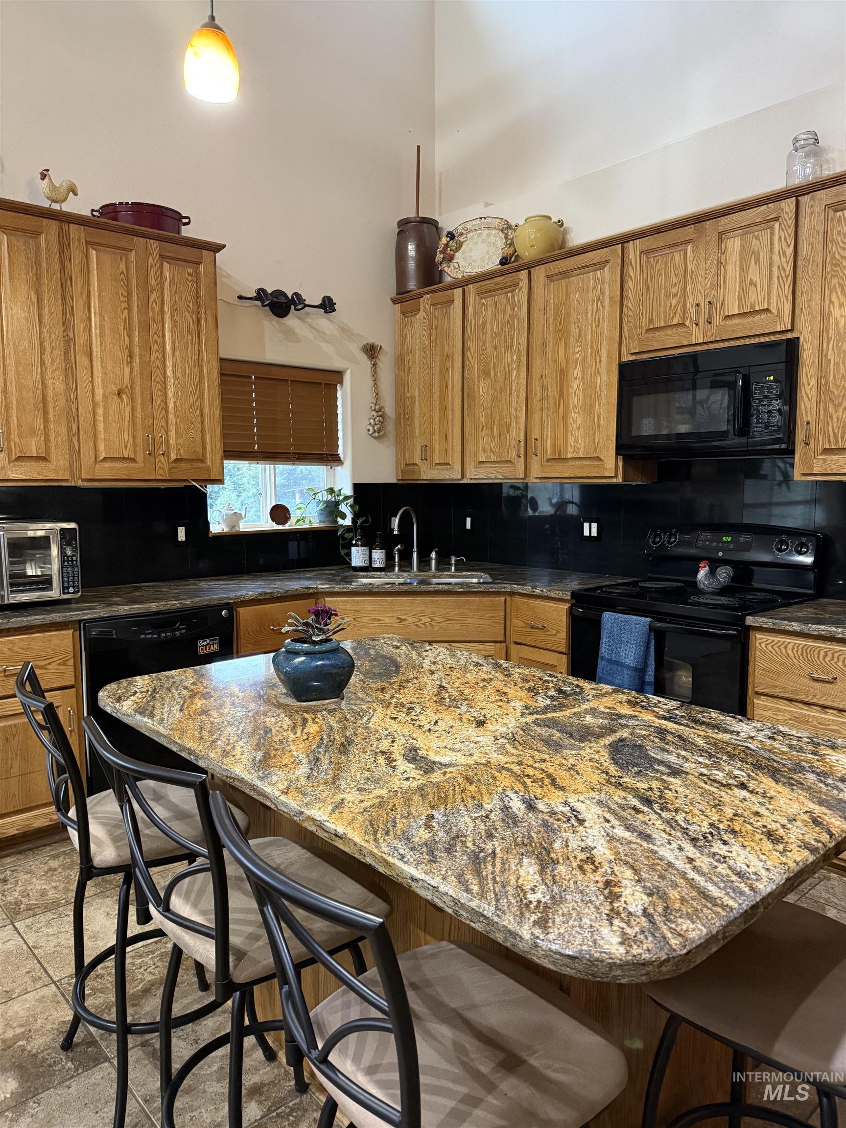 Kitchen with a kitchen breakfast bar, brown cabinets, black appliances, dark stone counters, and a center island