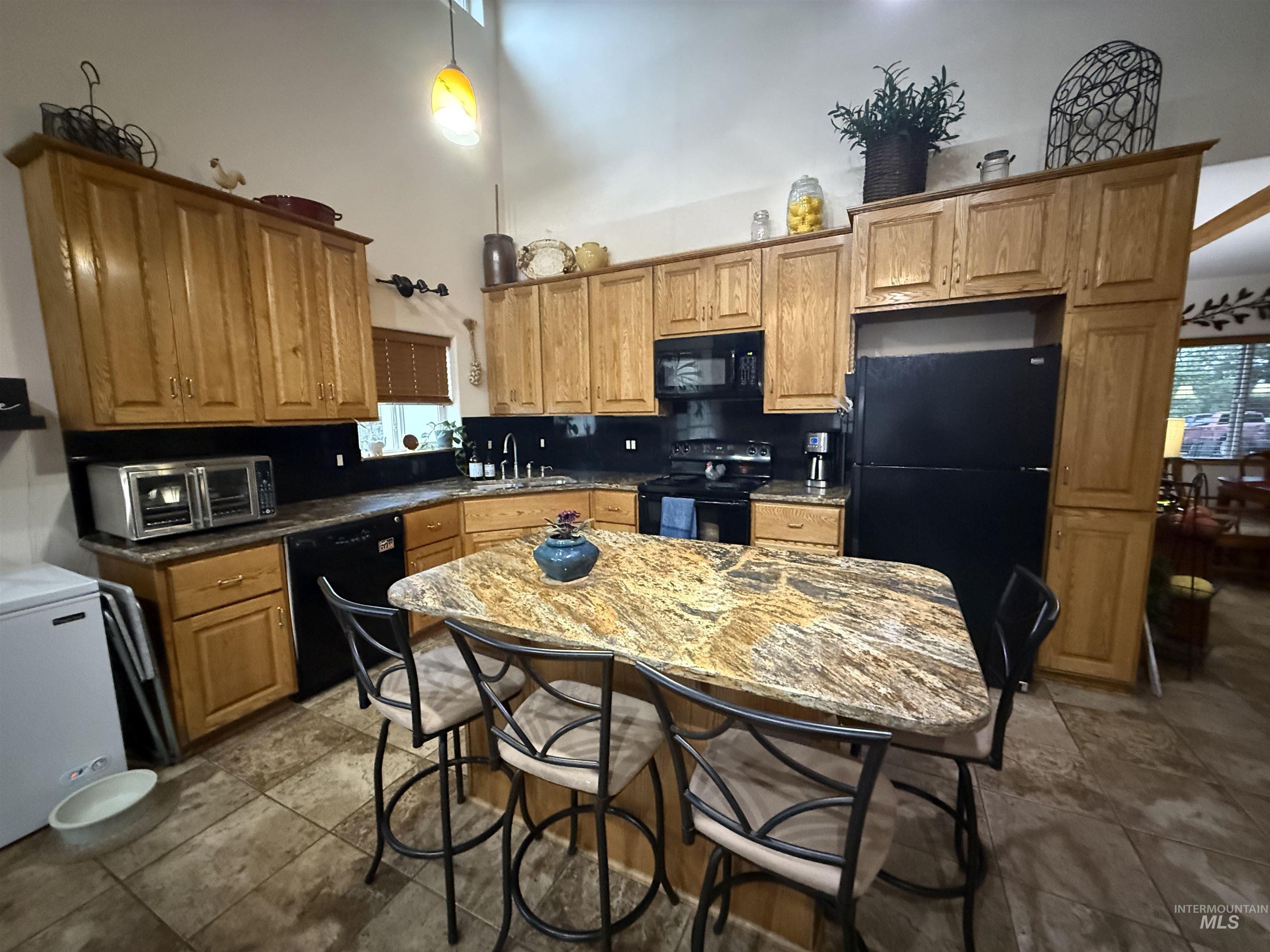 Kitchen with a towering ceiling, a breakfast bar, black appliances, brown cabinets, and a kitchen island