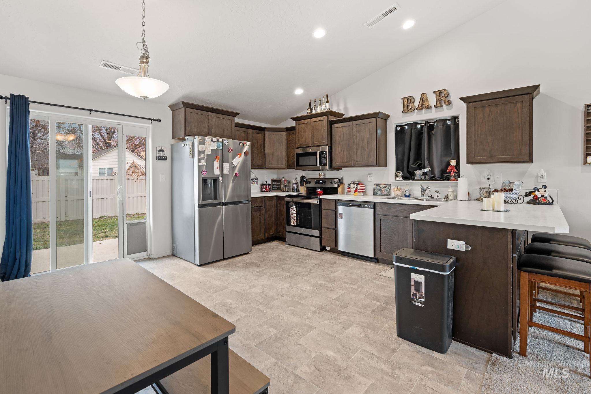 Kitchen featuring dark brown cabinetry, a peninsula, appliances with stainless steel finishes, light countertops, and a breakfast bar