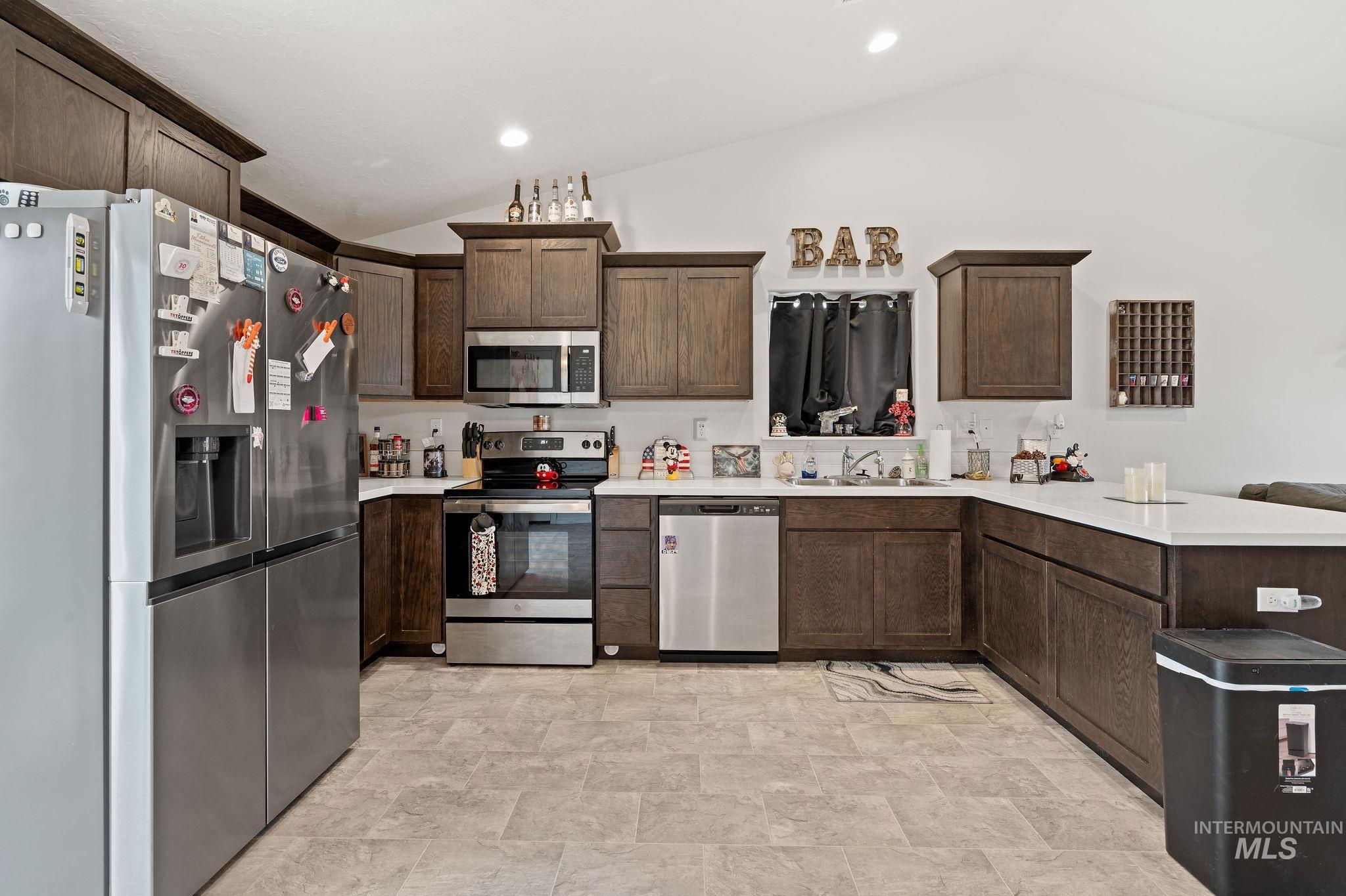 Kitchen with appliances with stainless steel finishes, lofted ceiling, a peninsula, dark brown cabinets, and stone finish flooring