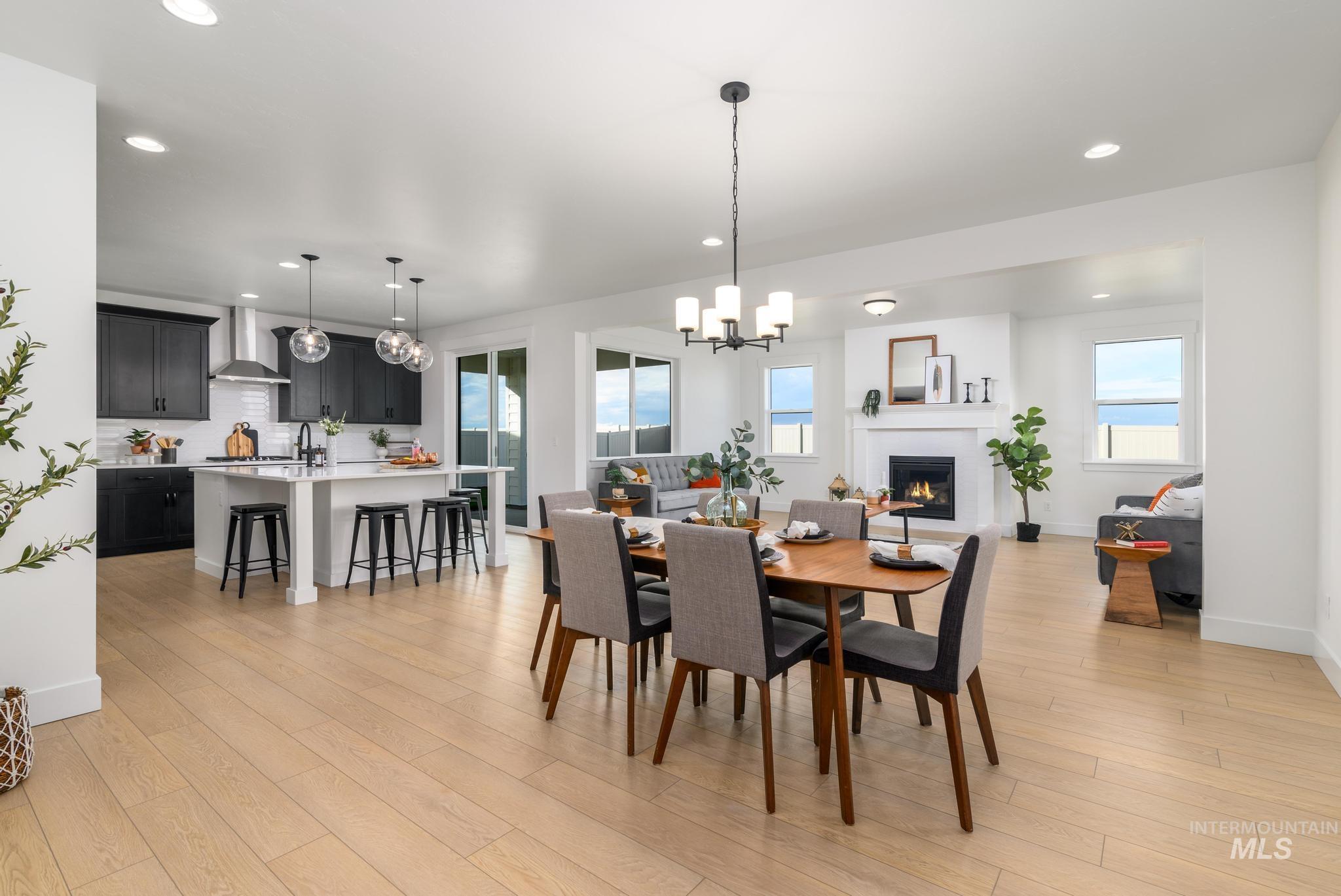 Dining area with recessed lighting, a warm lit fireplace, light wood-style floors, and a chandelier