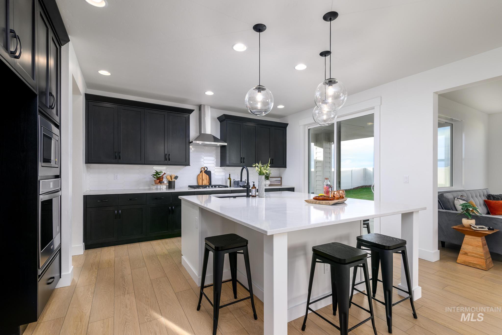 Kitchen with dark cabinetry, a kitchen bar, light stone counters, a kitchen island with sink, and hanging light fixtures