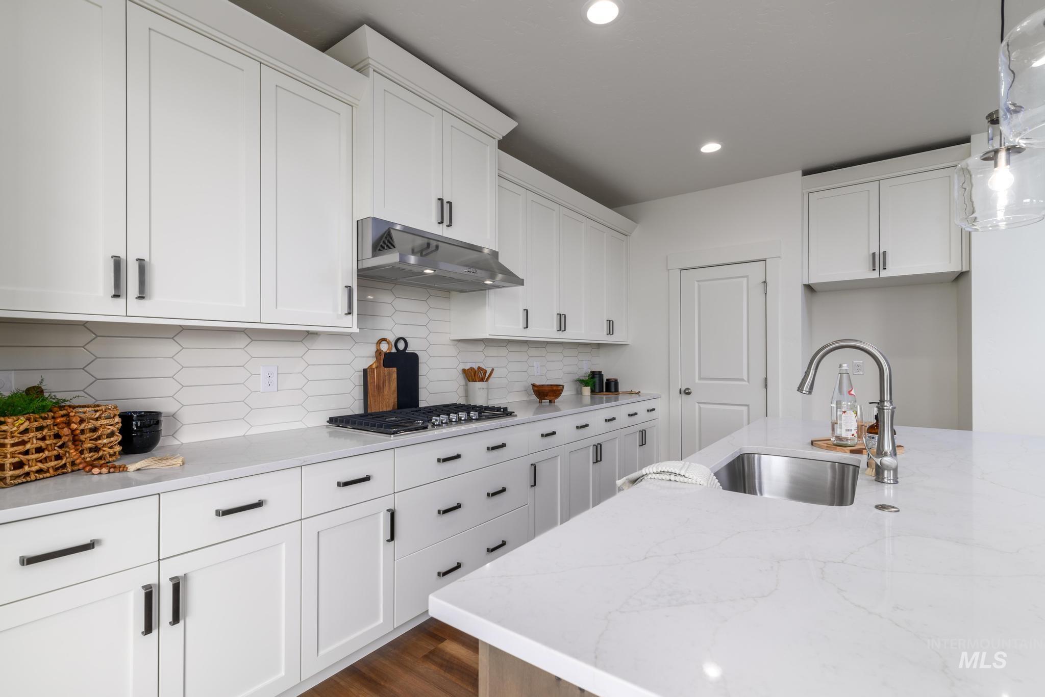 Kitchen featuring white cabinetry, light stone countertops, hanging light fixtures, under cabinet range hood, and recessed lighting