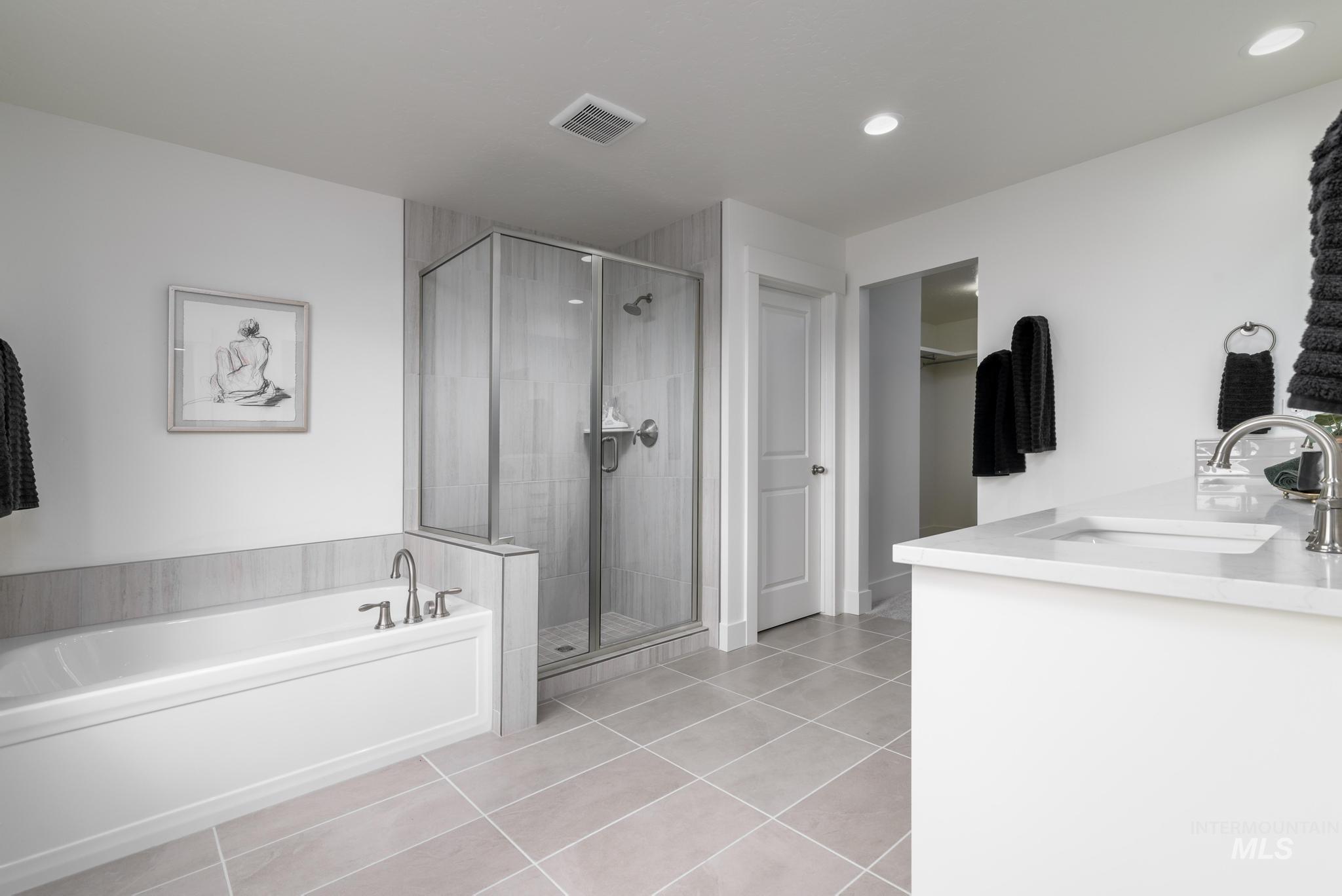 Full bathroom featuring a garden tub, a walk in closet, double vanity, light tile patterned floors, and a stall shower