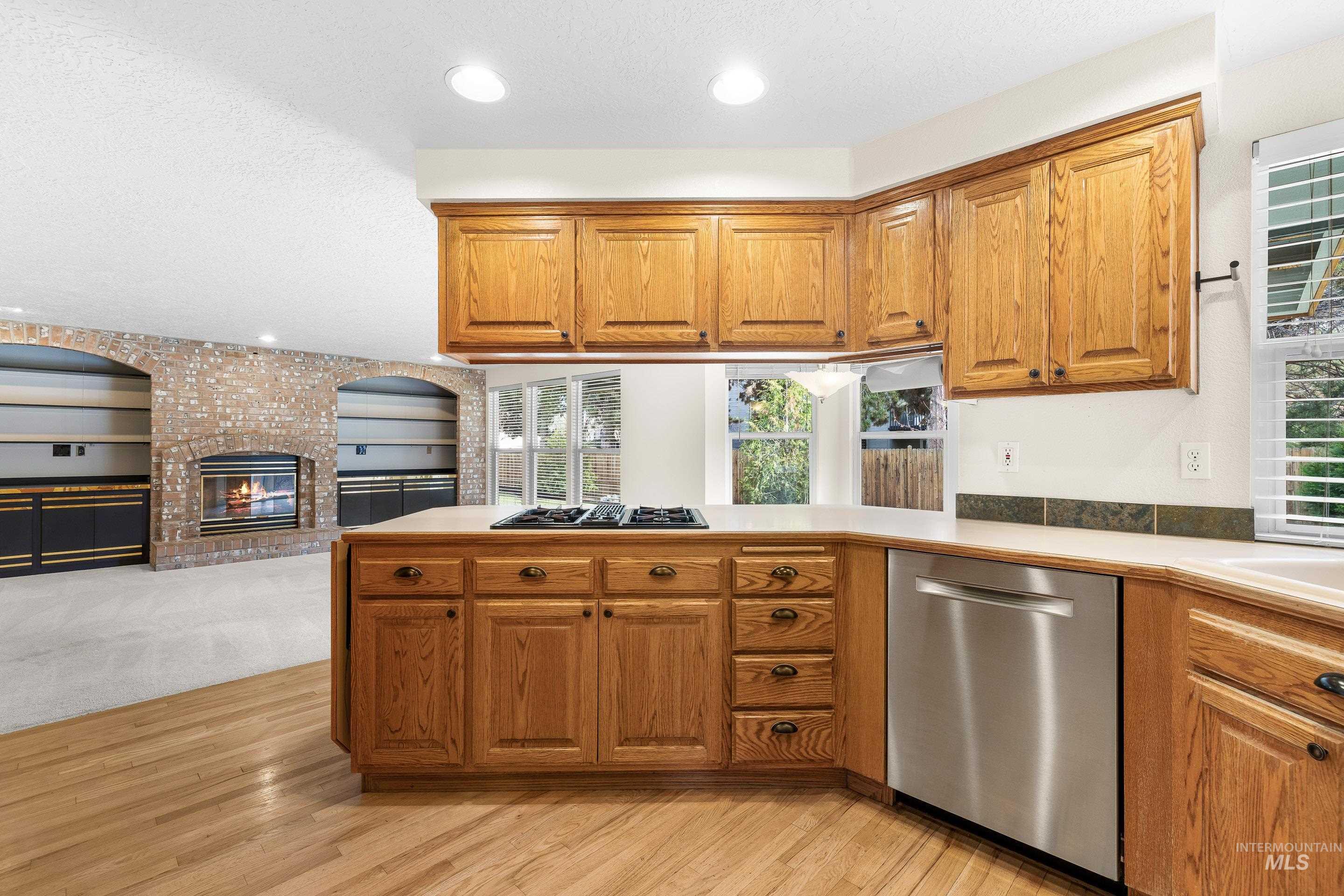 Kitchen with stainless steel dishwasher, open floor plan, brown cabinets, a peninsula, and a brick fireplace