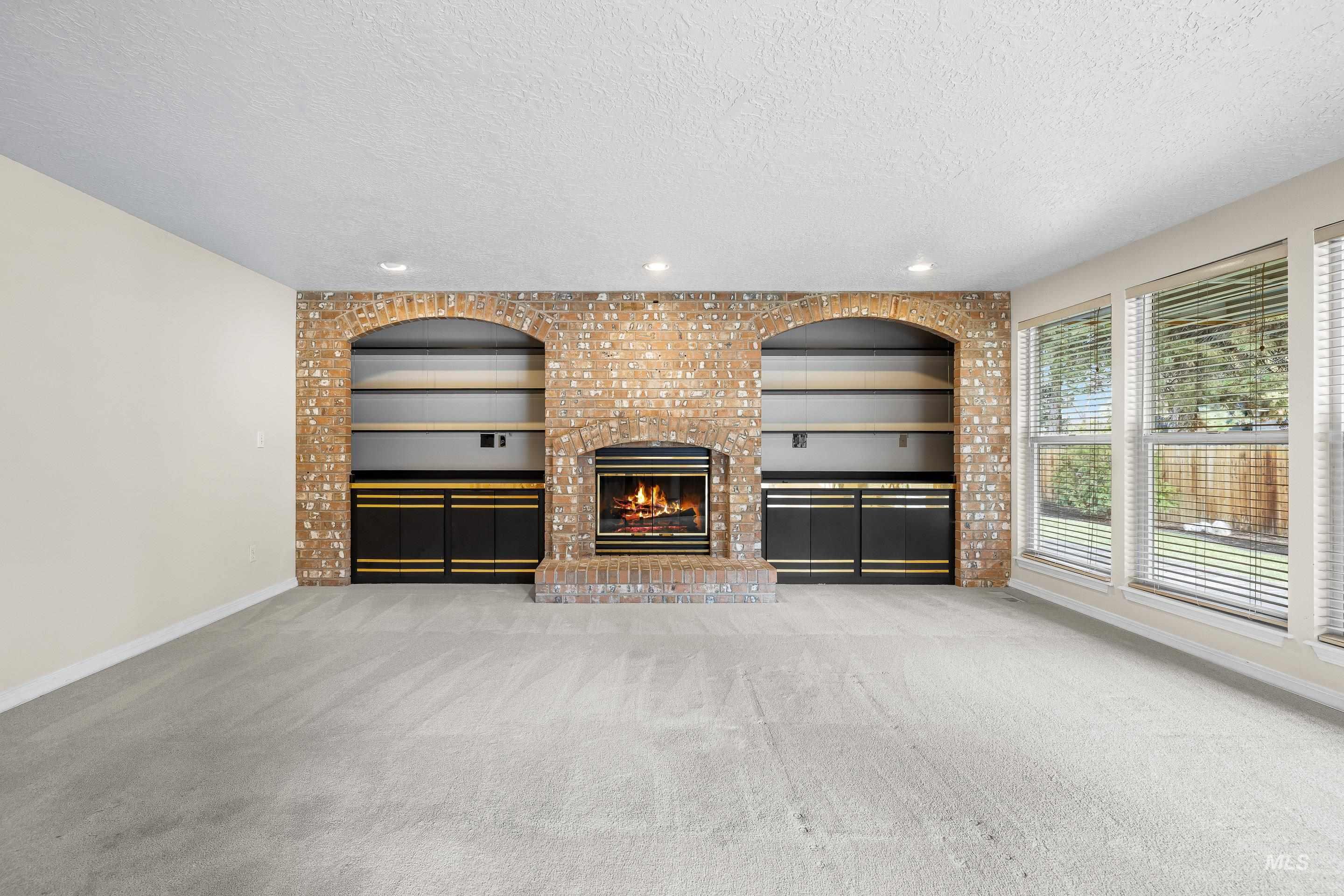 Unfurnished living room featuring built in shelves, a brick fireplace, a textured ceiling, carpet floors, and recessed lighting