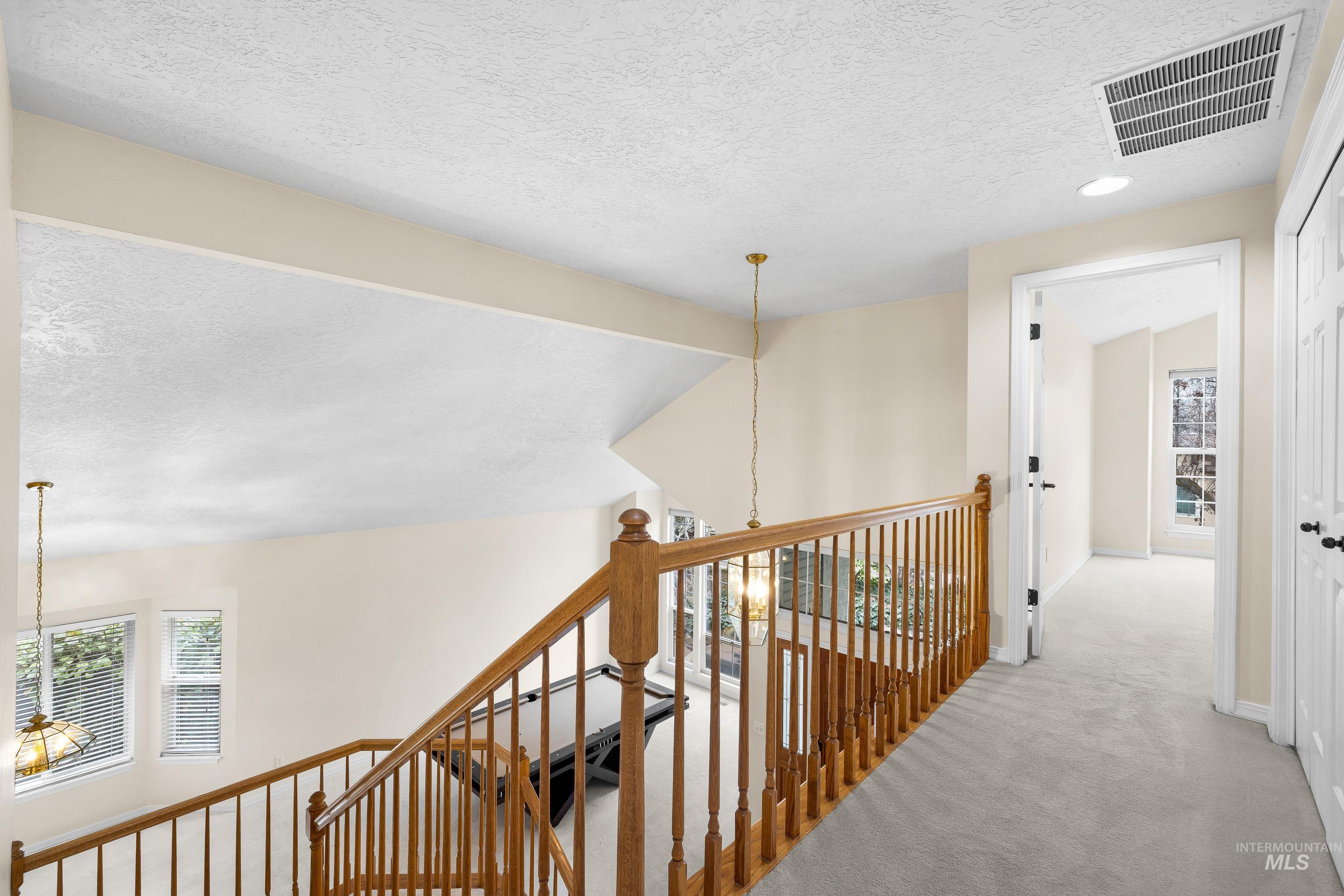 Hallway with a textured ceiling, a chandelier, carpet flooring, and an upstairs landing