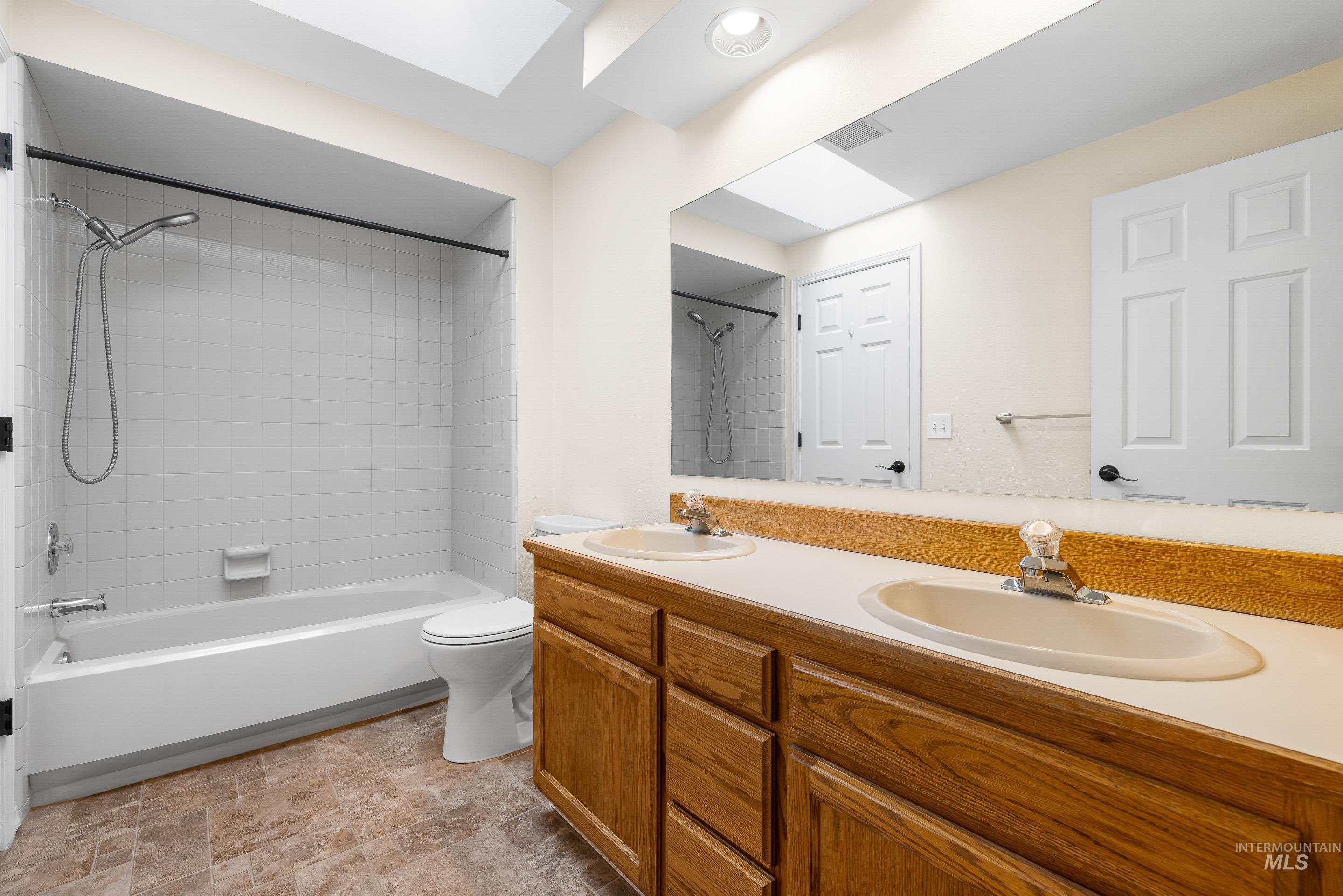 Full bathroom featuring double vanity, washtub / shower combination, and stone finish floors