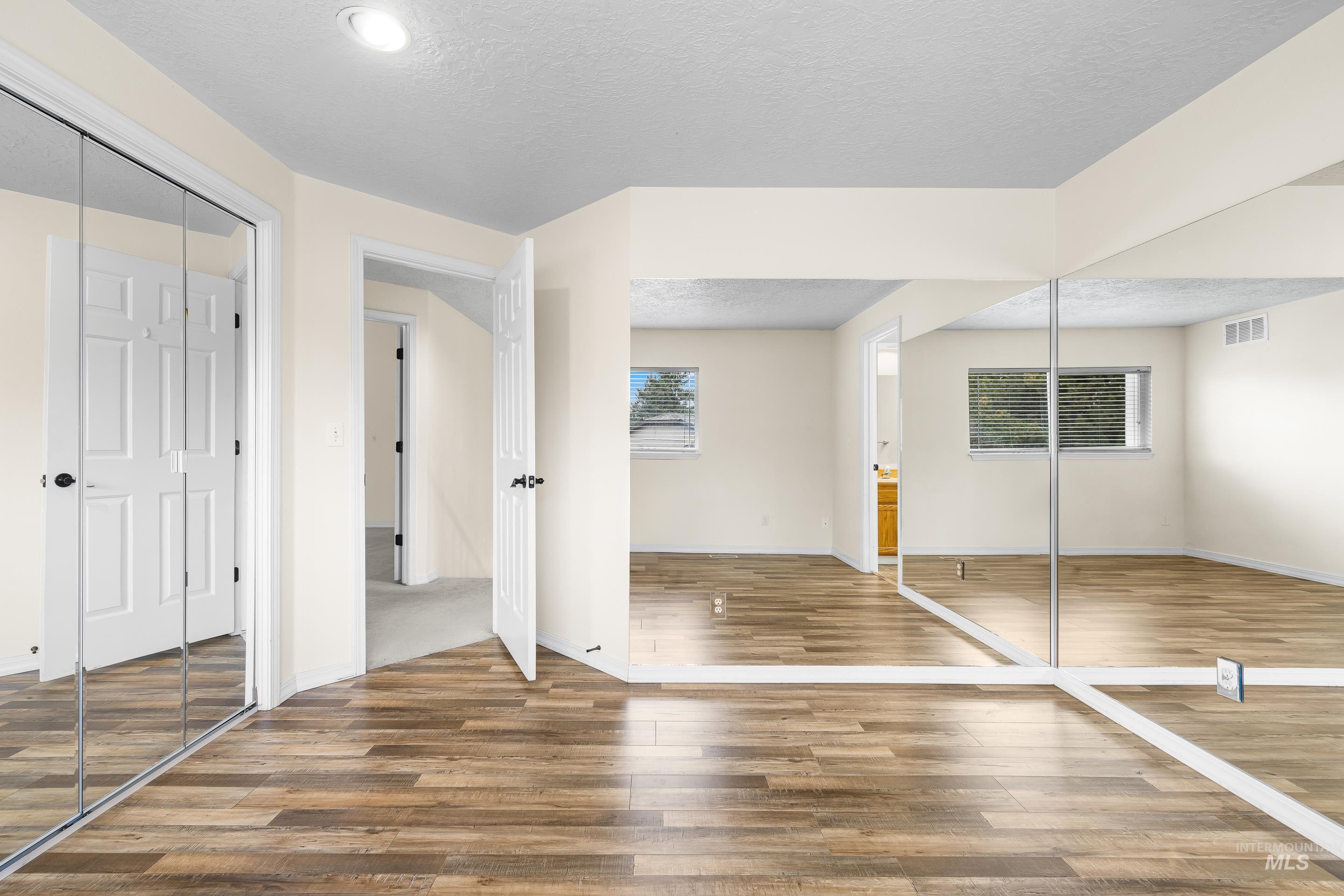Unfurnished bedroom with a closet, a textured ceiling, ensuite bath, and wood finished floors