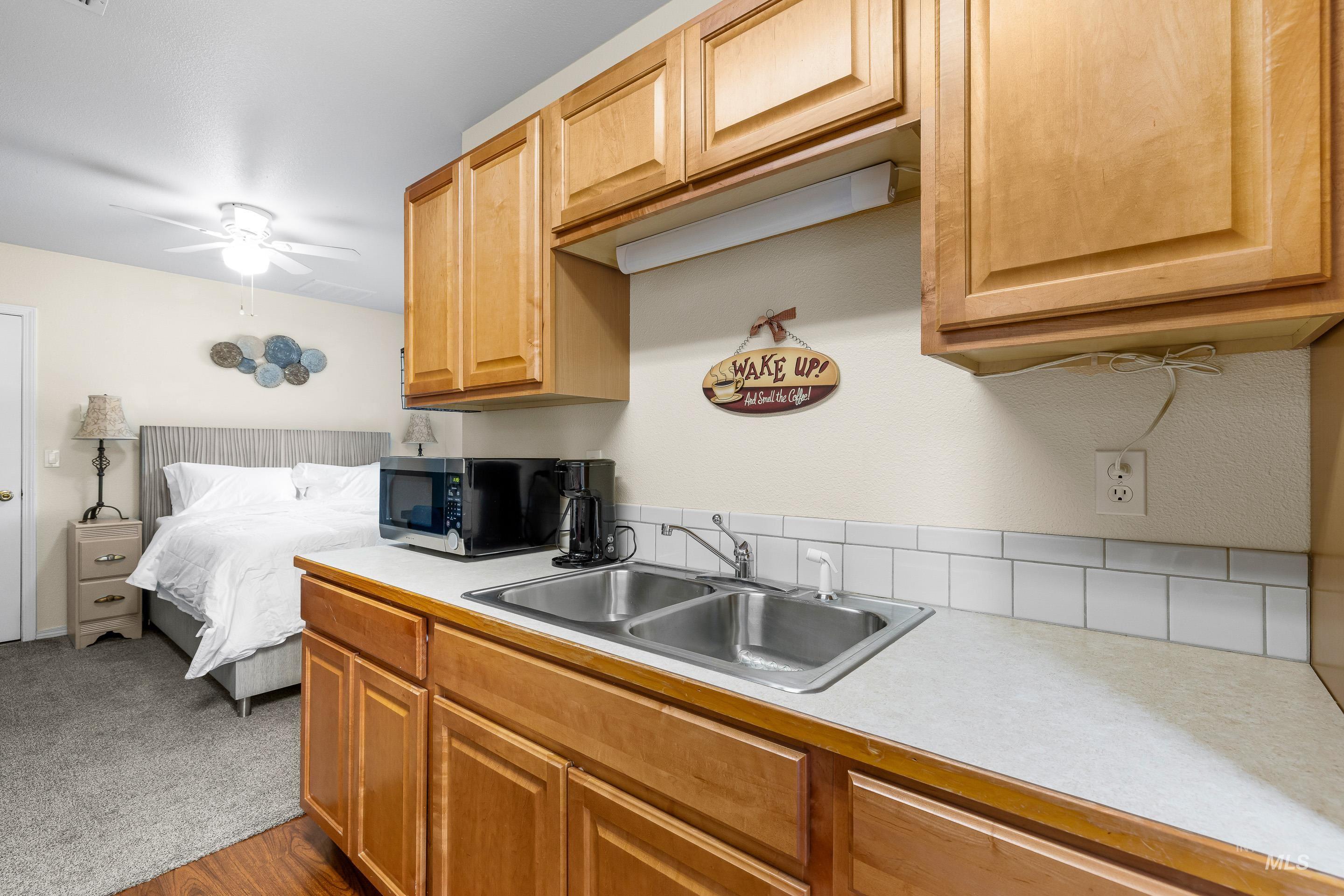 Kitchen featuring light countertops, stainless steel microwave, a ceiling fan, and dark colored carpet