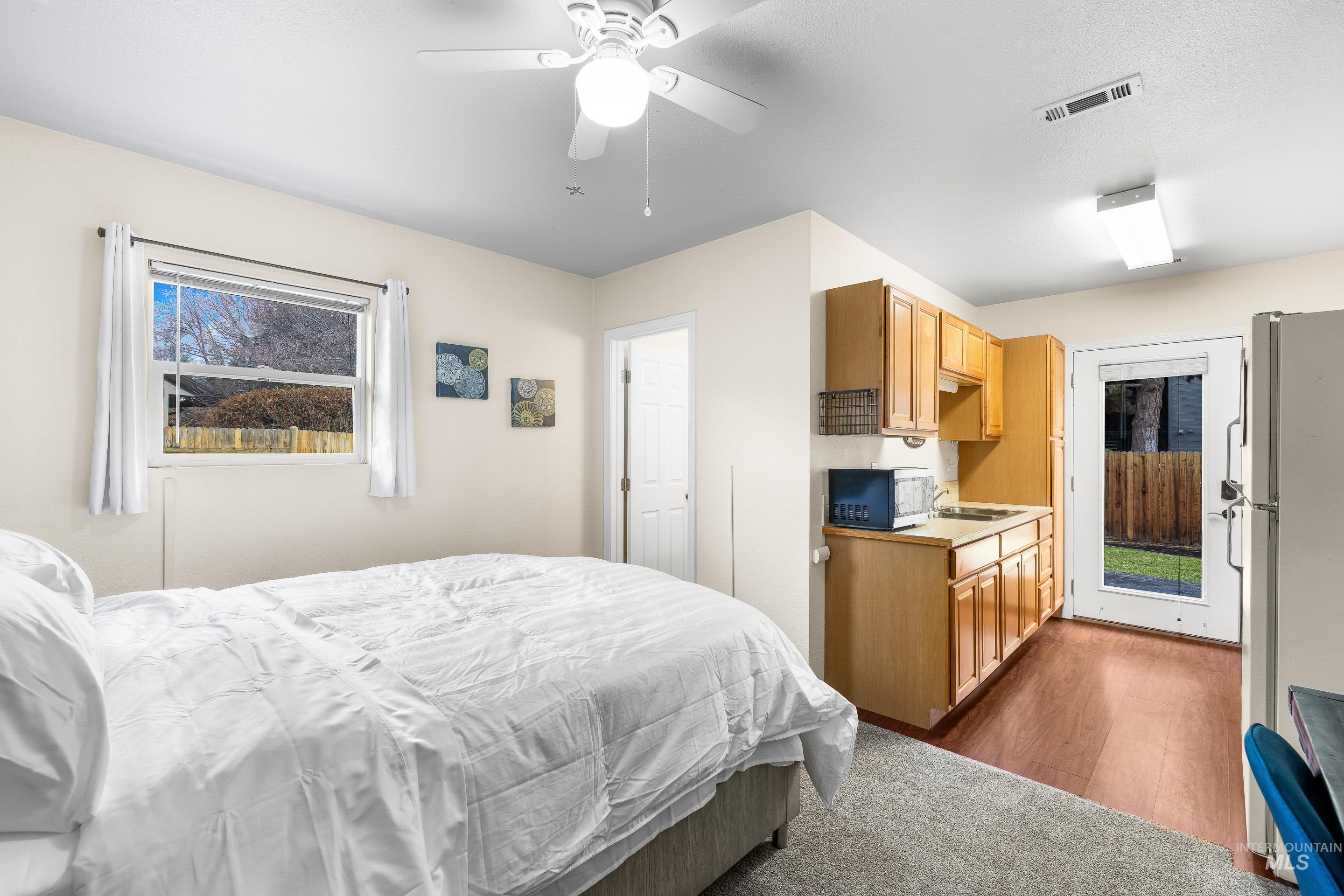 Bedroom with multiple windows, freestanding refrigerator, a ceiling fan, and dark wood-type flooring