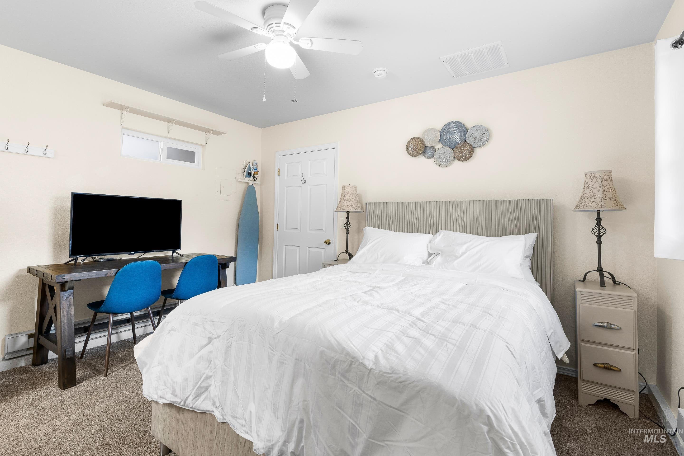 Carpeted bedroom with ceiling fan, an office area, and a baseboard radiator