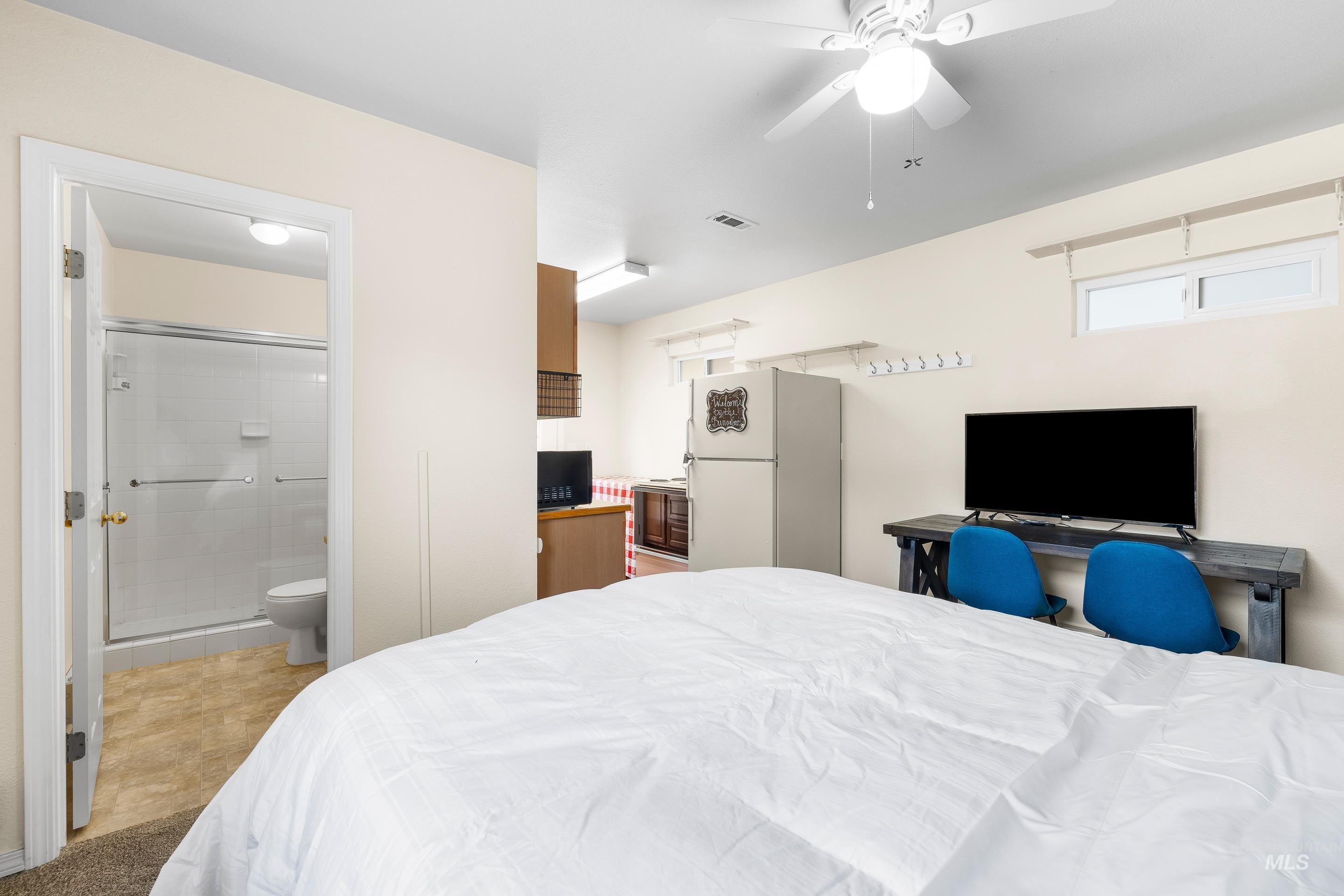 Bedroom with freestanding refrigerator, ceiling fan, and a desk